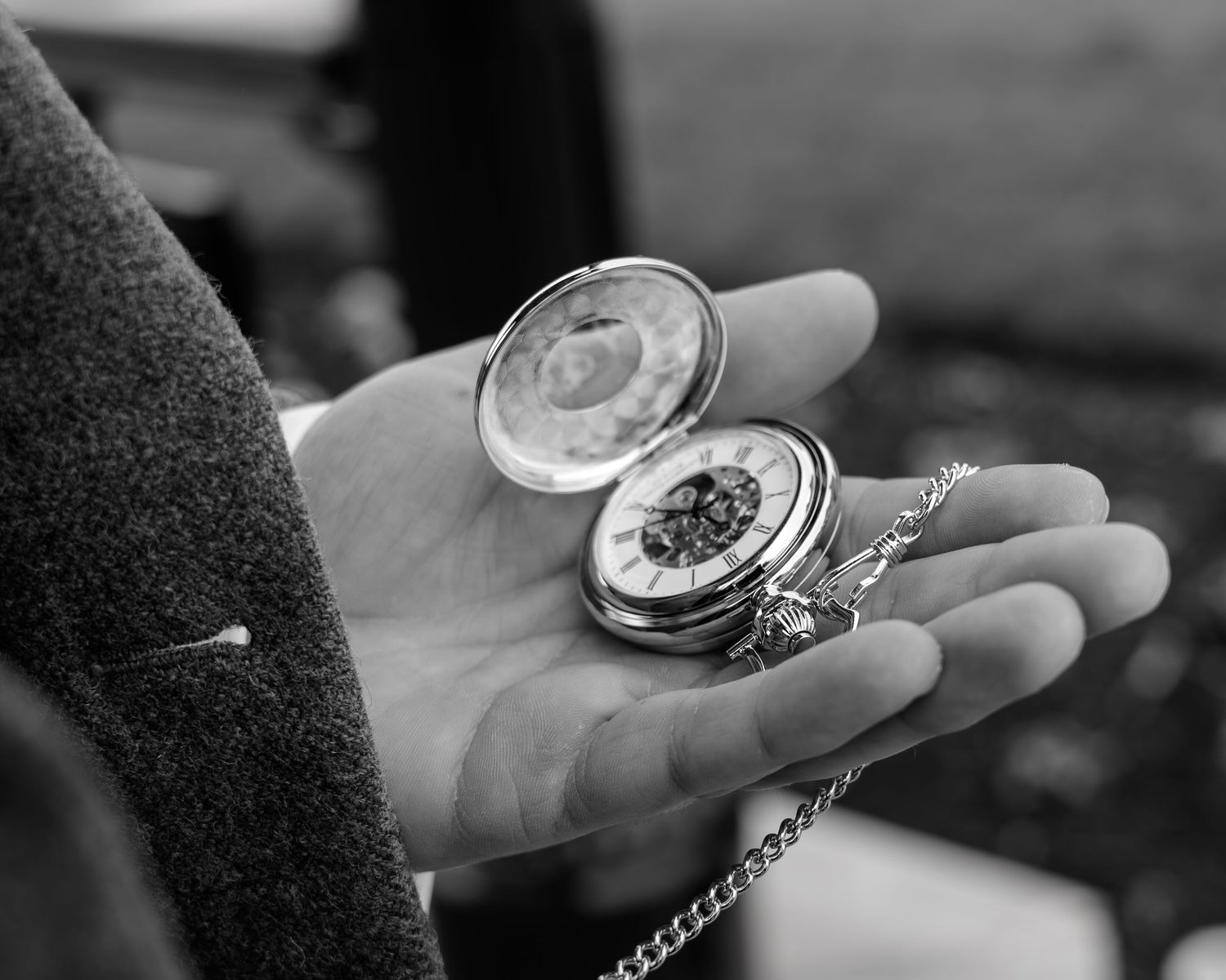 A close-up sequence of hands holding and opening an antique pocket watch with a chain in black and white.