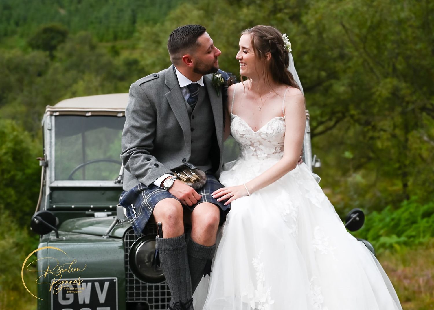 A classic vintage vehicle serves as a backdrop for a romantic wedding portrait in lush green surroundings. Carrick Castle.