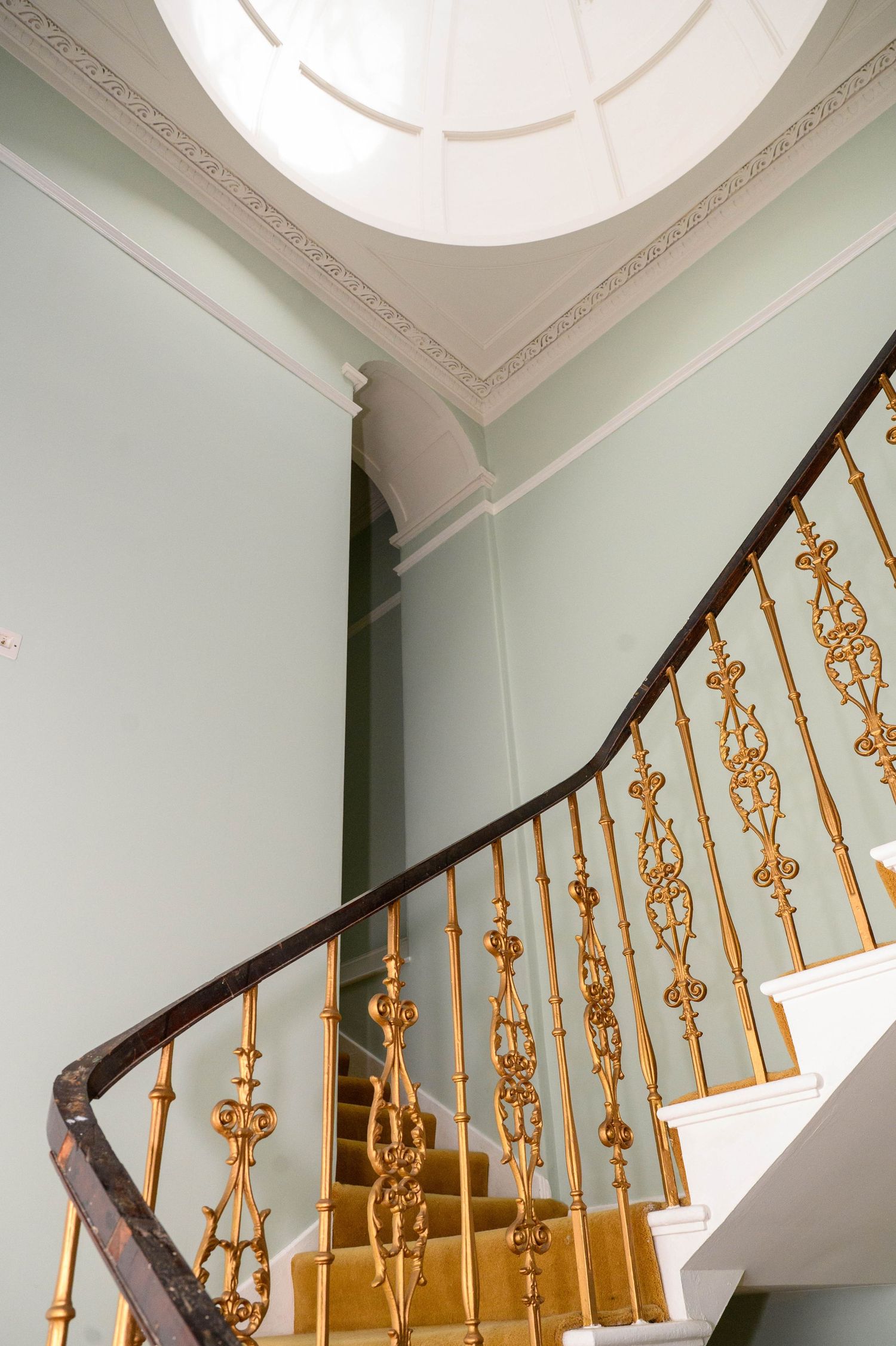Elegant curved staircase with ornate gold balusters and dark handrail beneath a decorative white ceiling medallion.