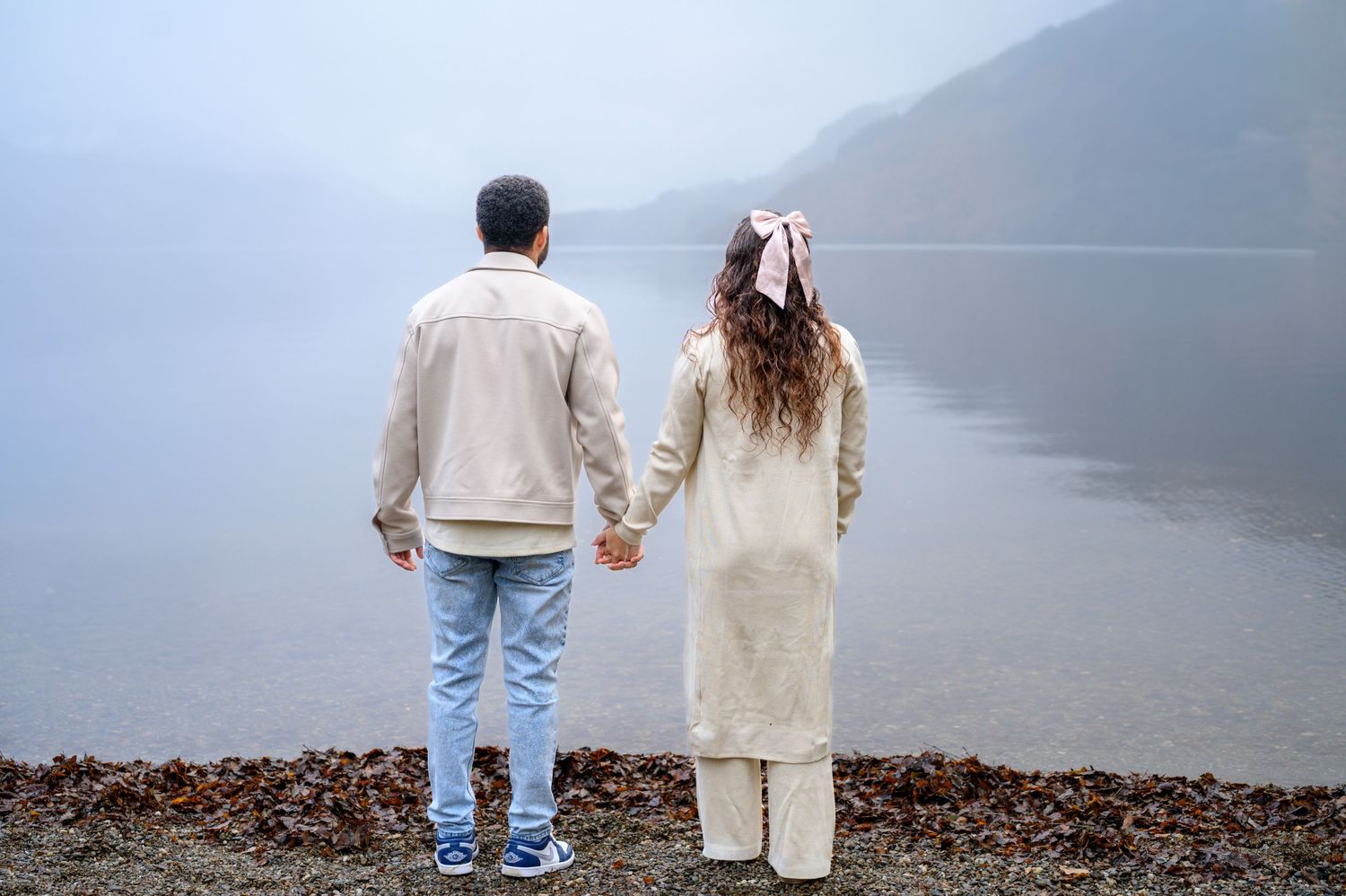 Couple in casual attire walking together along a misty shoreline on a foggy morning. Loch Lomond.