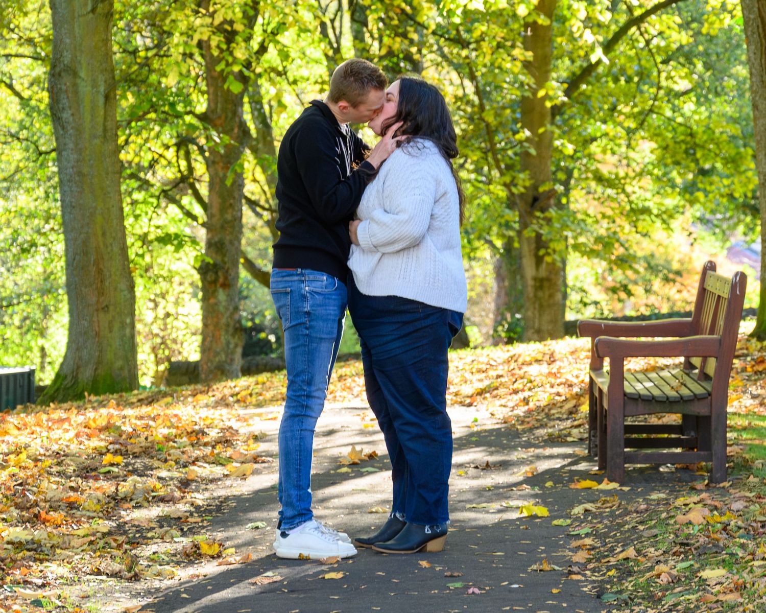 Couple sharing romantic moment in autumn park with fallen leaves scattered on pathway. Linlithgow Palace.