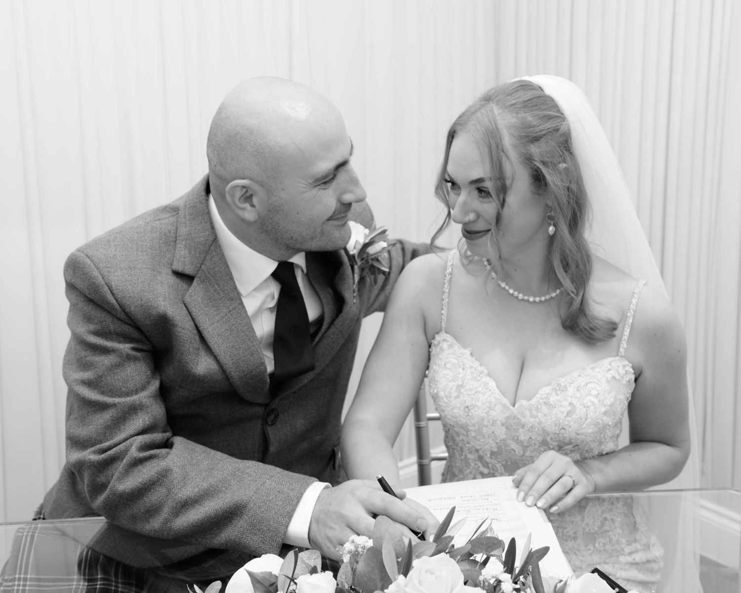 Black and white photo of a bride and groom smiling at each other while cutting their wedding cake.