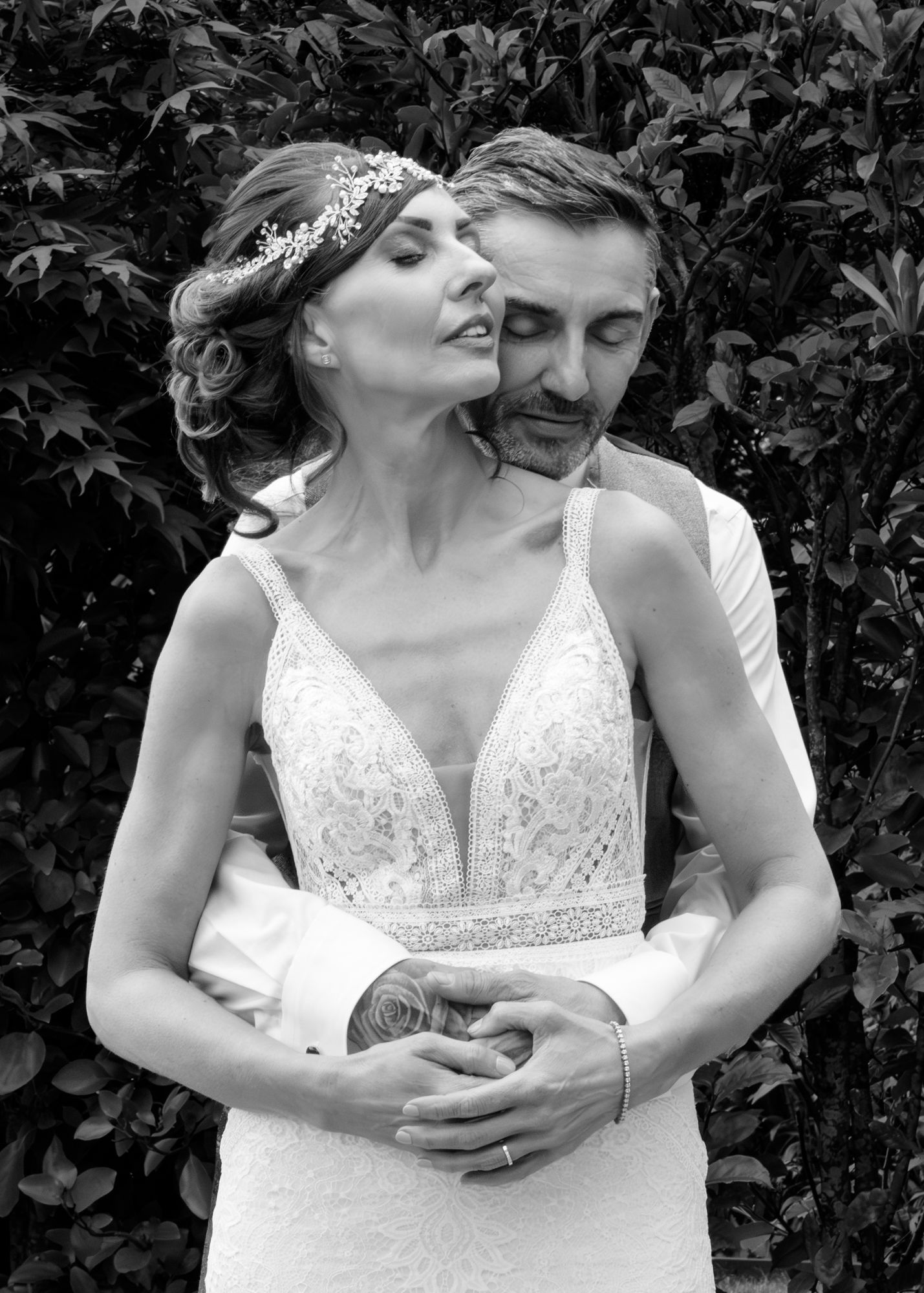A romantic couple in wedding attire embraces in front of a leafy green background, shown in a series of intimate poses. Dalziel Park