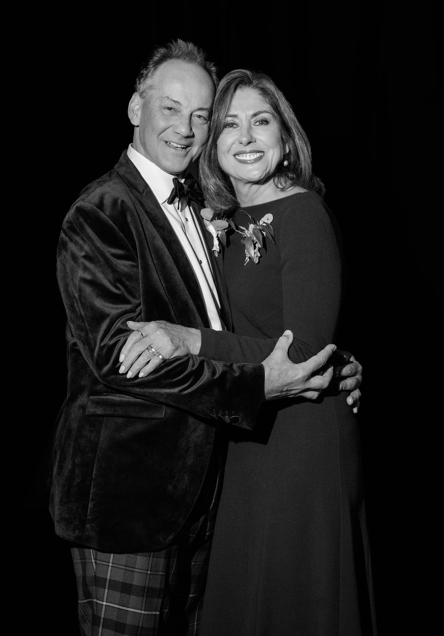 Black and white photo of an elegant couple embracing and smiling at a formal event.