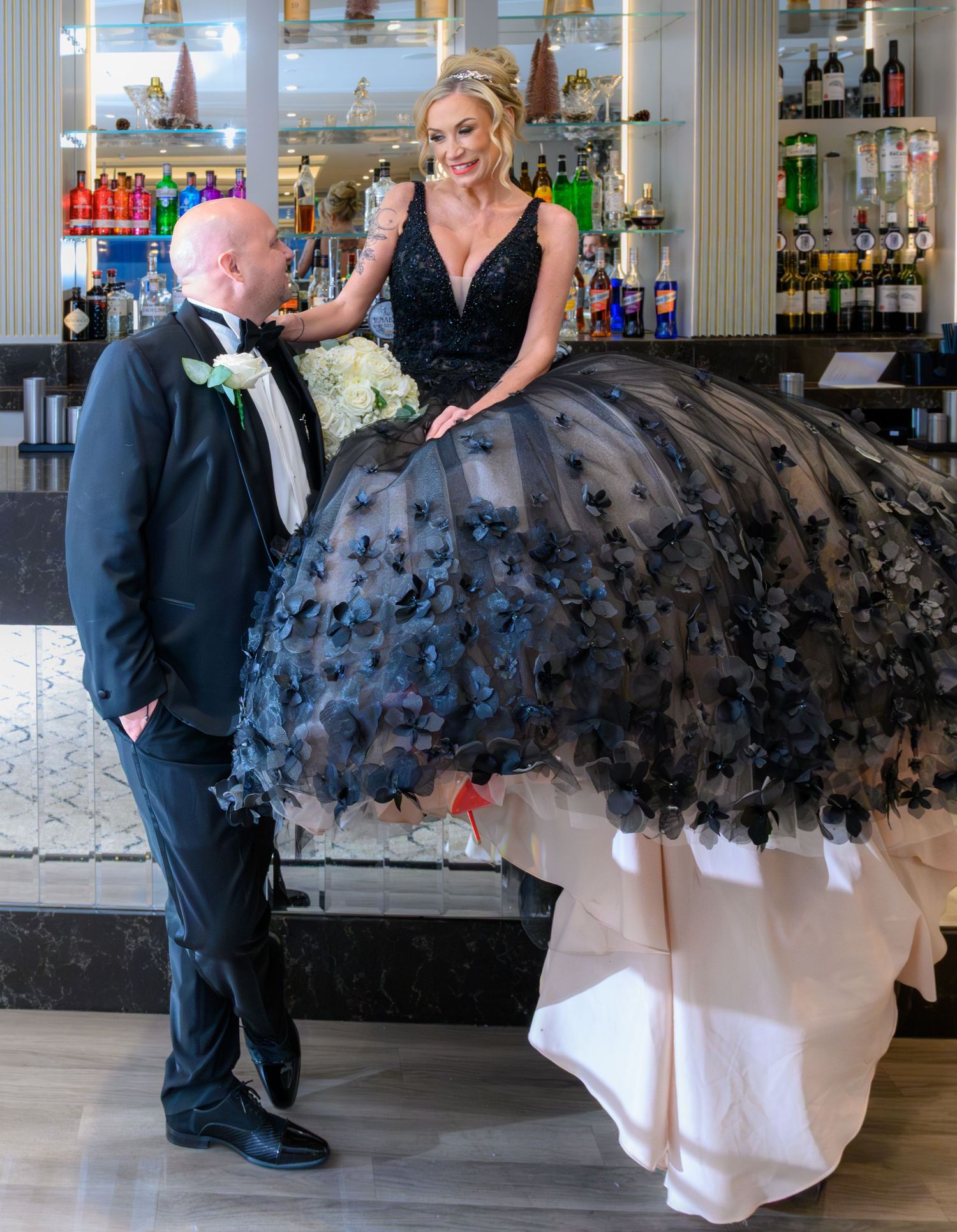 A couple shares a playful moment at a bar, with the woman wearing an elegant black tulle dress with white underlay. Seamill Hydro in Ayshire