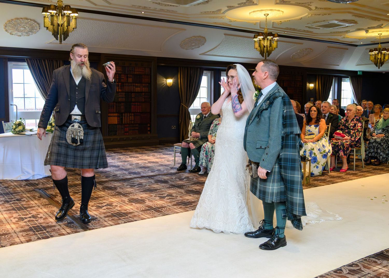 Scottish wedding ceremony with bride, groom in tartan kilt, and bagpiper performing in elegant venue.