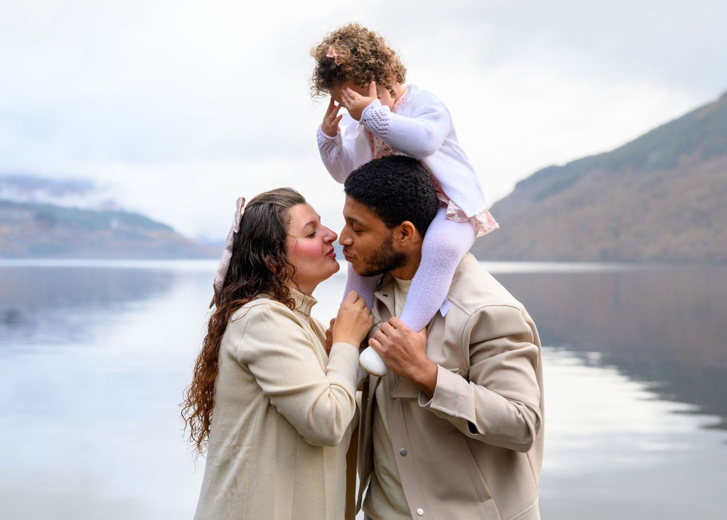 A couple shares romantic moments by a misty lake with mountains in the background during their engagement photo session. Loch Lomond.