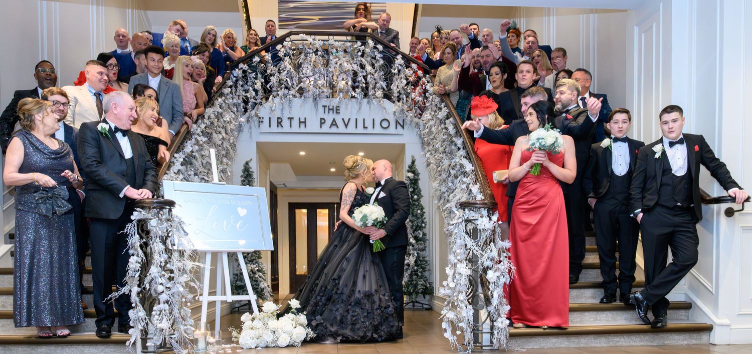 Wedding guests react with joy and excitement during an emotional moment at an elegant indoor reception ceremony. Seamill Hydro