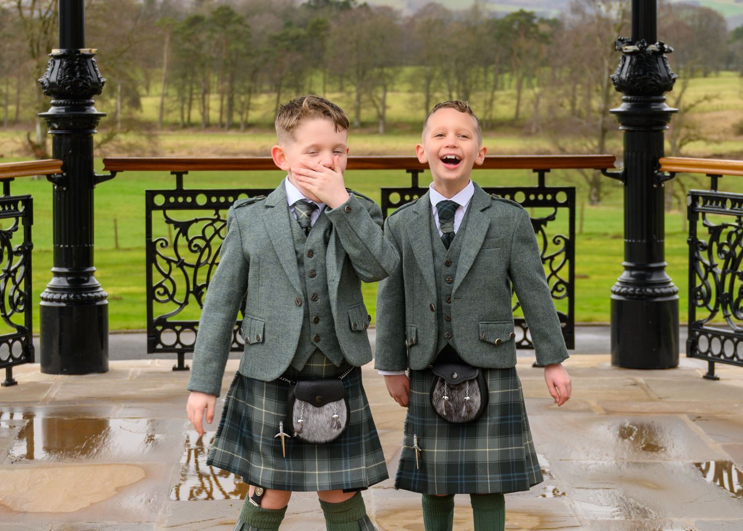 Two students in school uniforms walk together holding hands and laughing in a park setting.