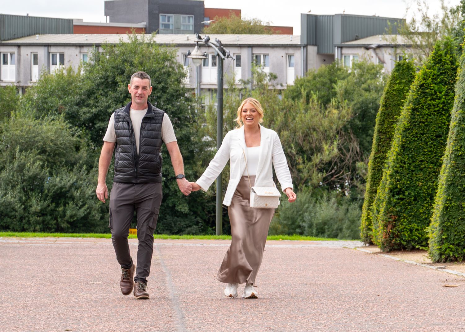 Couple walking hand in hand on a garden path surrounded by manicured hedges and greenery. Glasgow Green