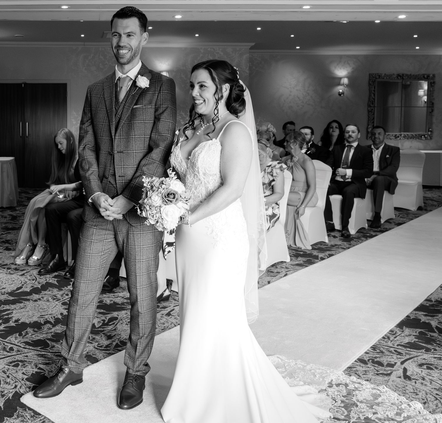 Black and white wedding ceremony photos showing a couple walking down a carpeted aisle surrounded by guests. Dalziel Park