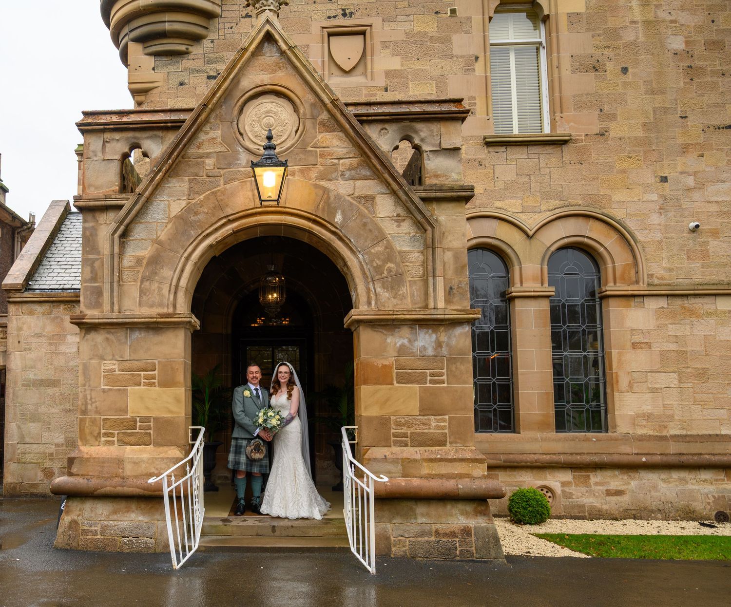 Bride and groom posing at the entrance of a historic stone church on their wedding day.