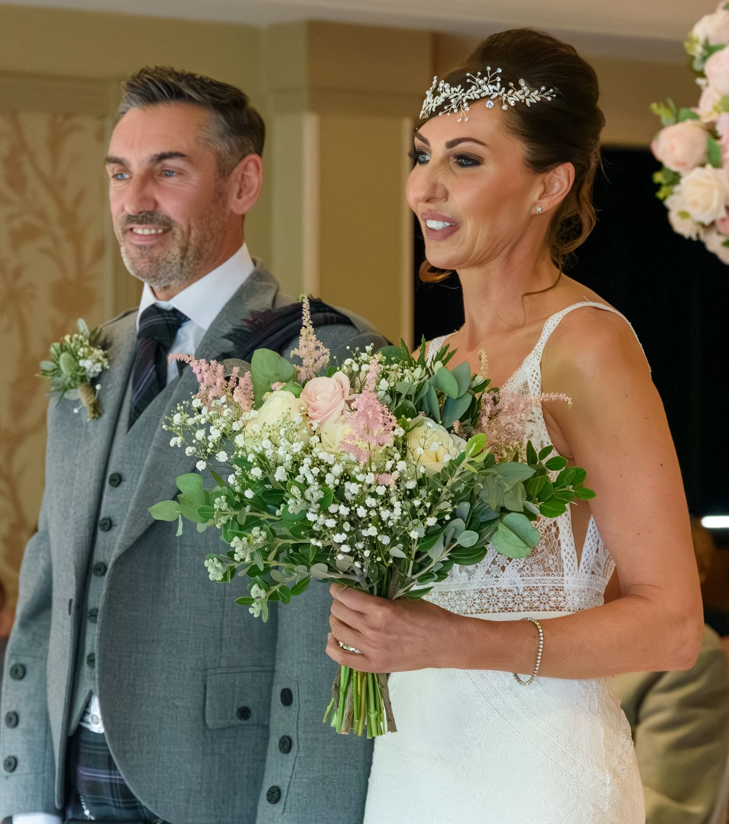 Joyful wedding couple sharing candid laughter while holding white floral bouquets in Dalziel Park, Motherwell