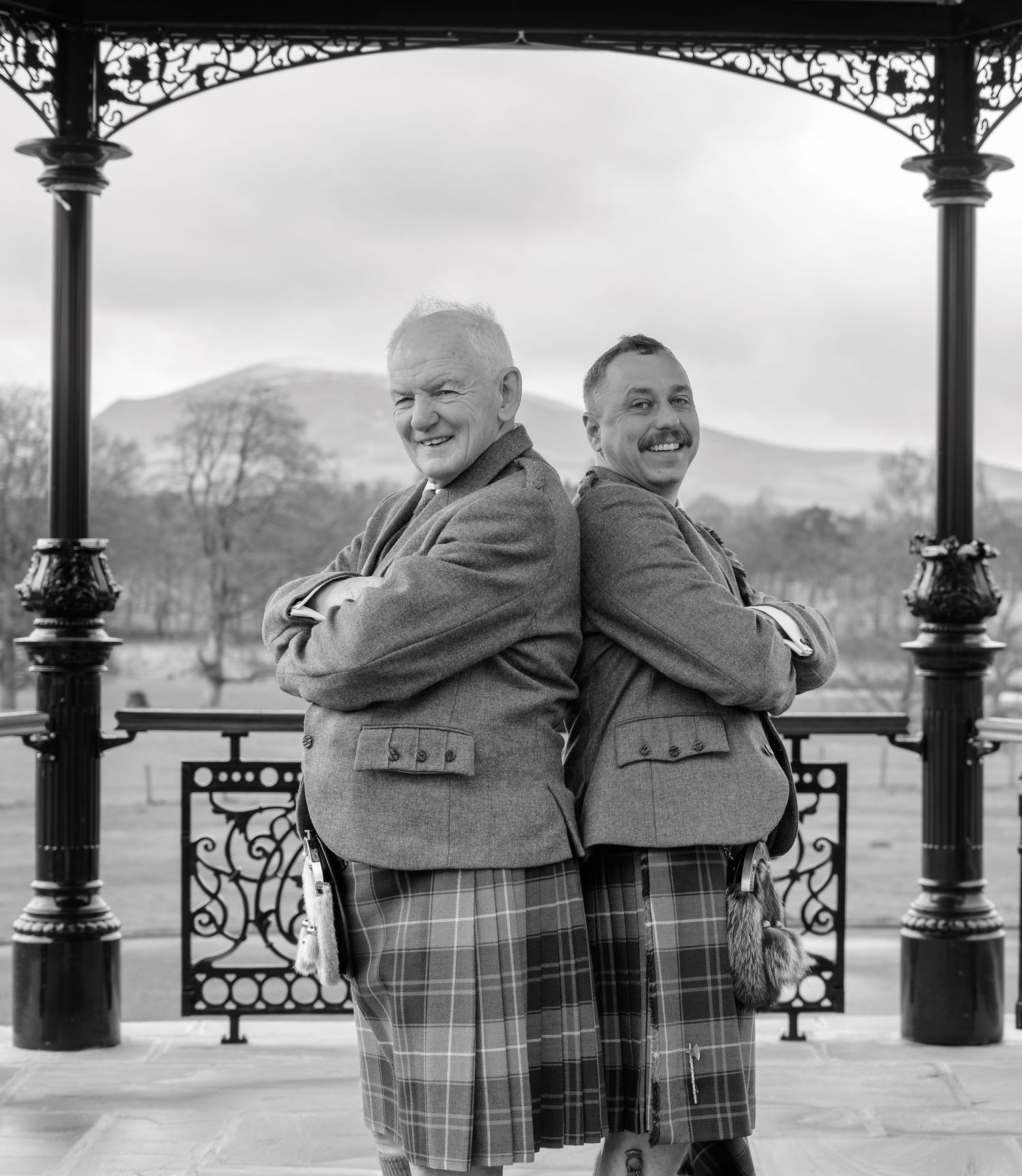 Three black and white photos show two people in plaid jackets embracing while standing on a scenic promenade.