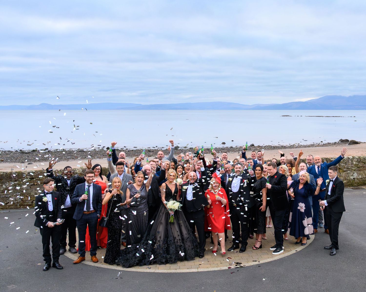 A panoramic sequence showing a large group of wedding guests celebrating by throwing confetti on a beach. Seamill Hydro