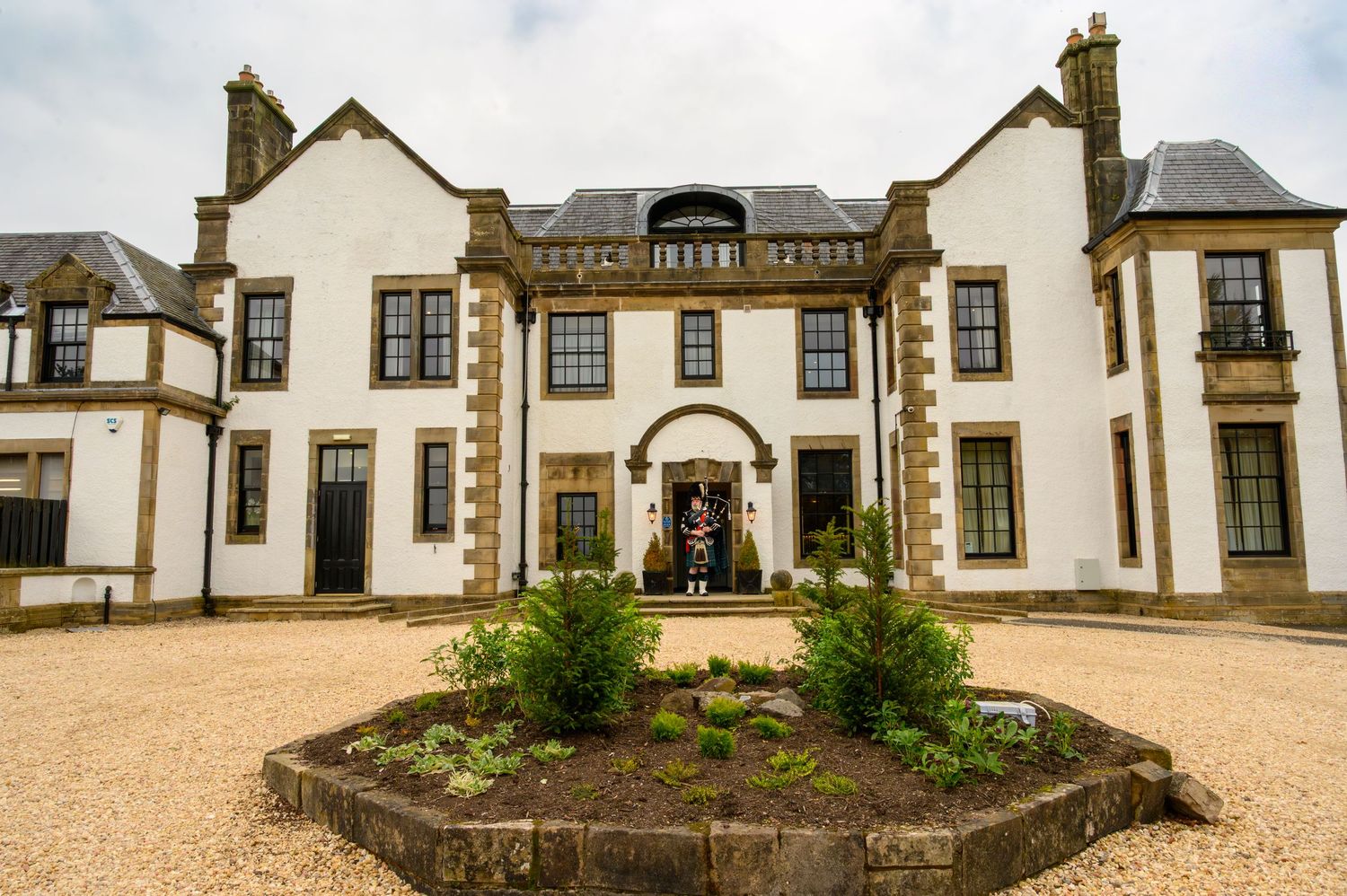 Grand white Scottish manor house with sandstone details, manicured garden bed, and ornate entrance doorway.