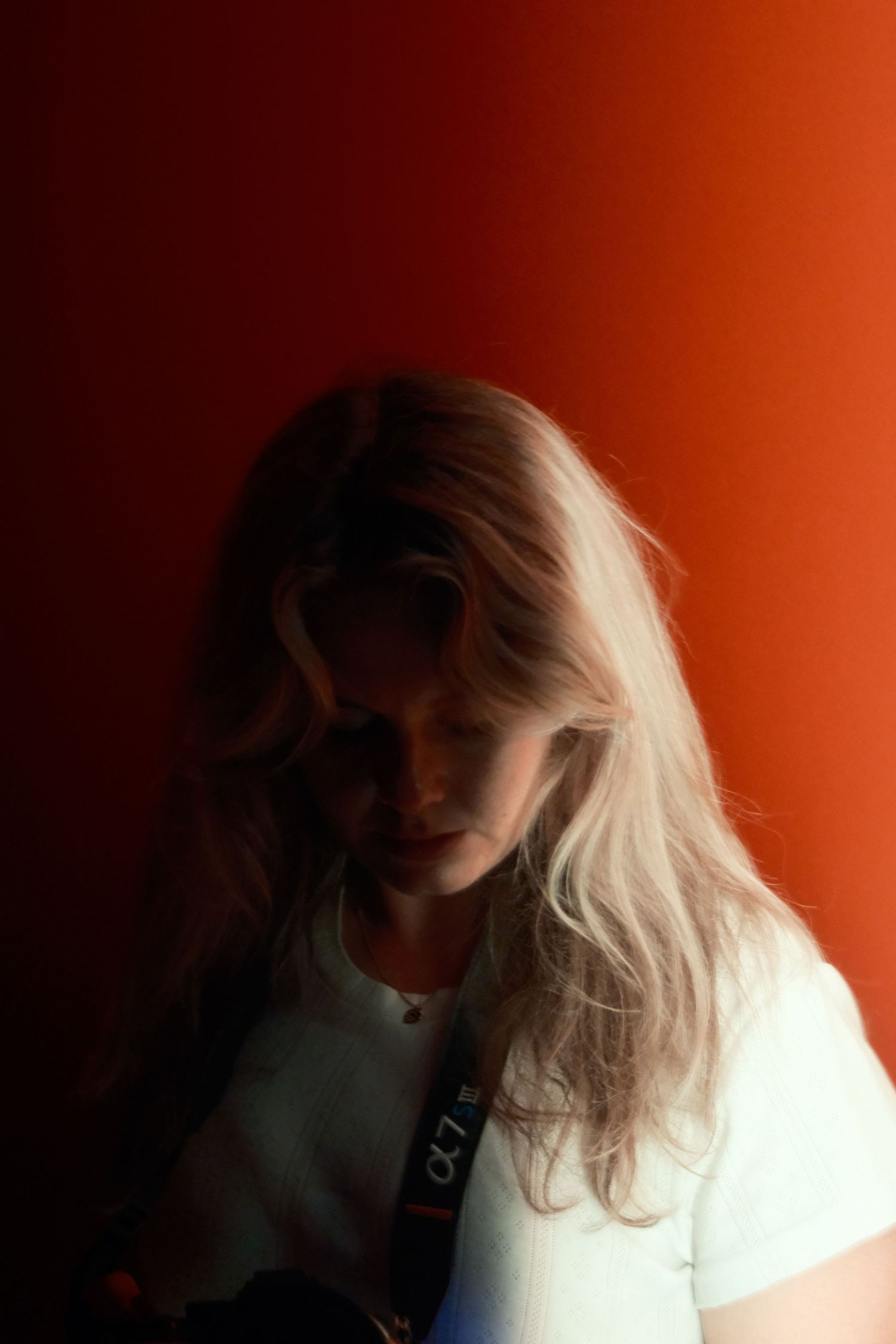 A woman standing agaisnt a wall, half of her face is black and the other half is red