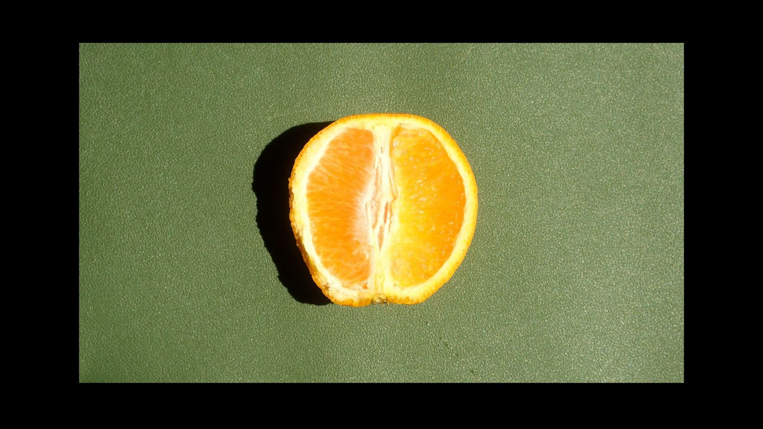Half an orange on a green mat with a thick black border