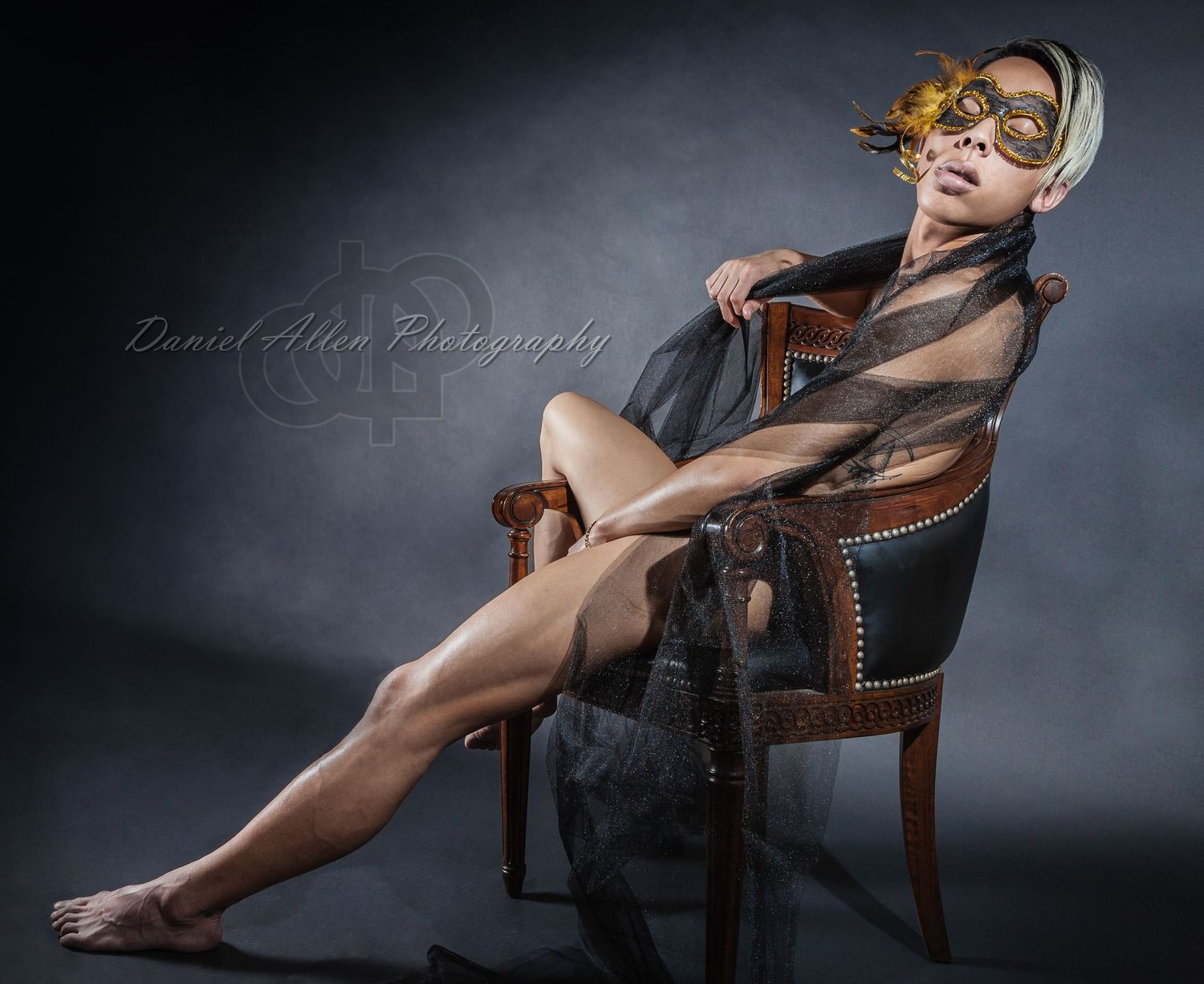 Artistic portrait with model in masquerade mask posed on leather chair.