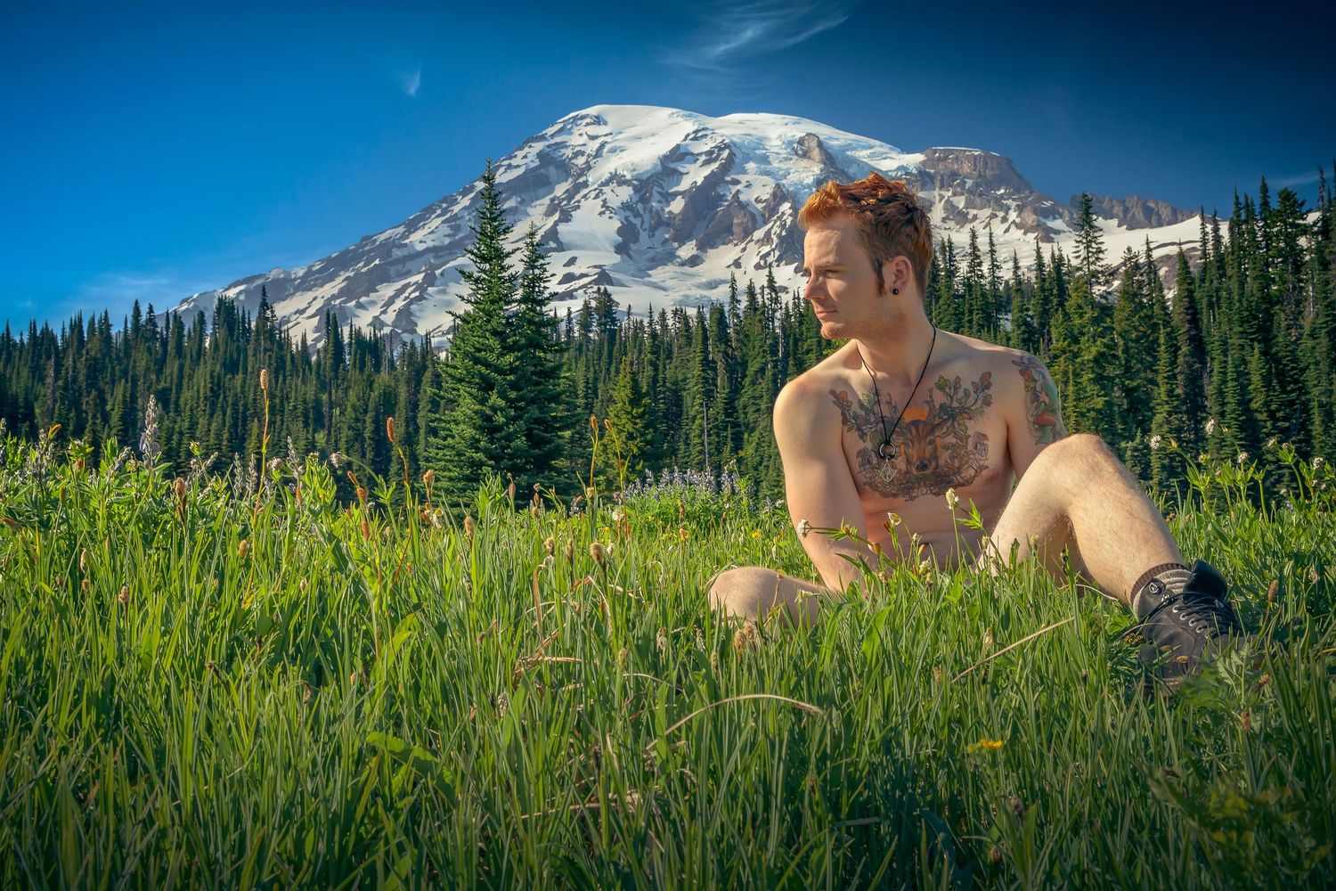 Person relaxing in alpine meadow with majestic Mount Rainier rising in the background.