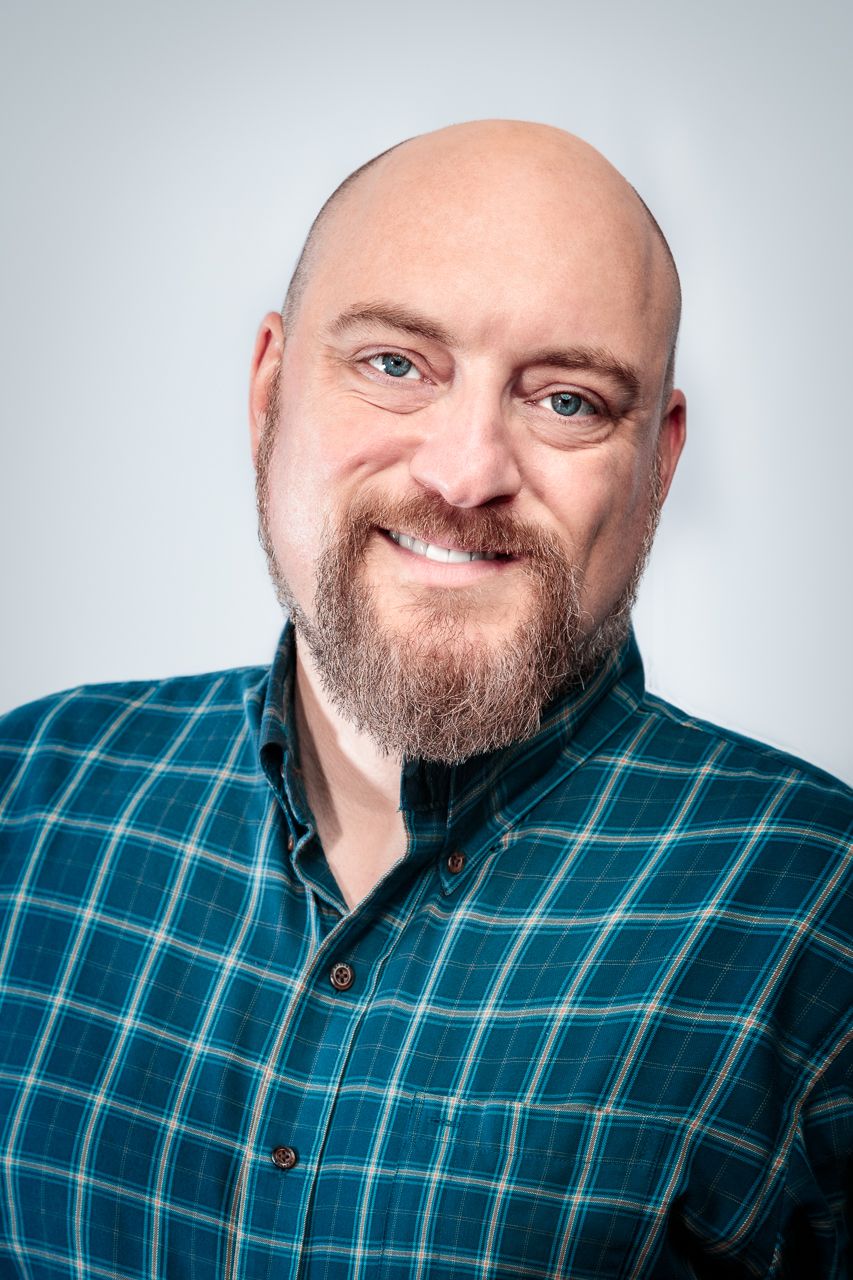 Casual portrait of a person in a teal plaid shirt against a white backdrop.