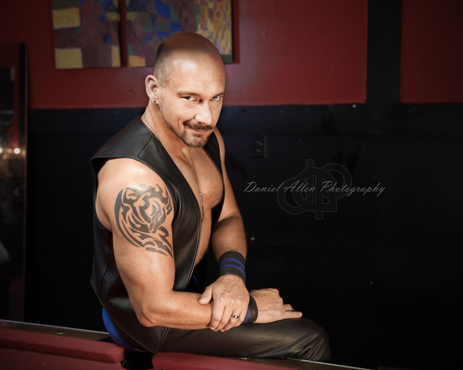 A person in a black sleeveless shirt poses for a dramatic photo series against a dark red background.