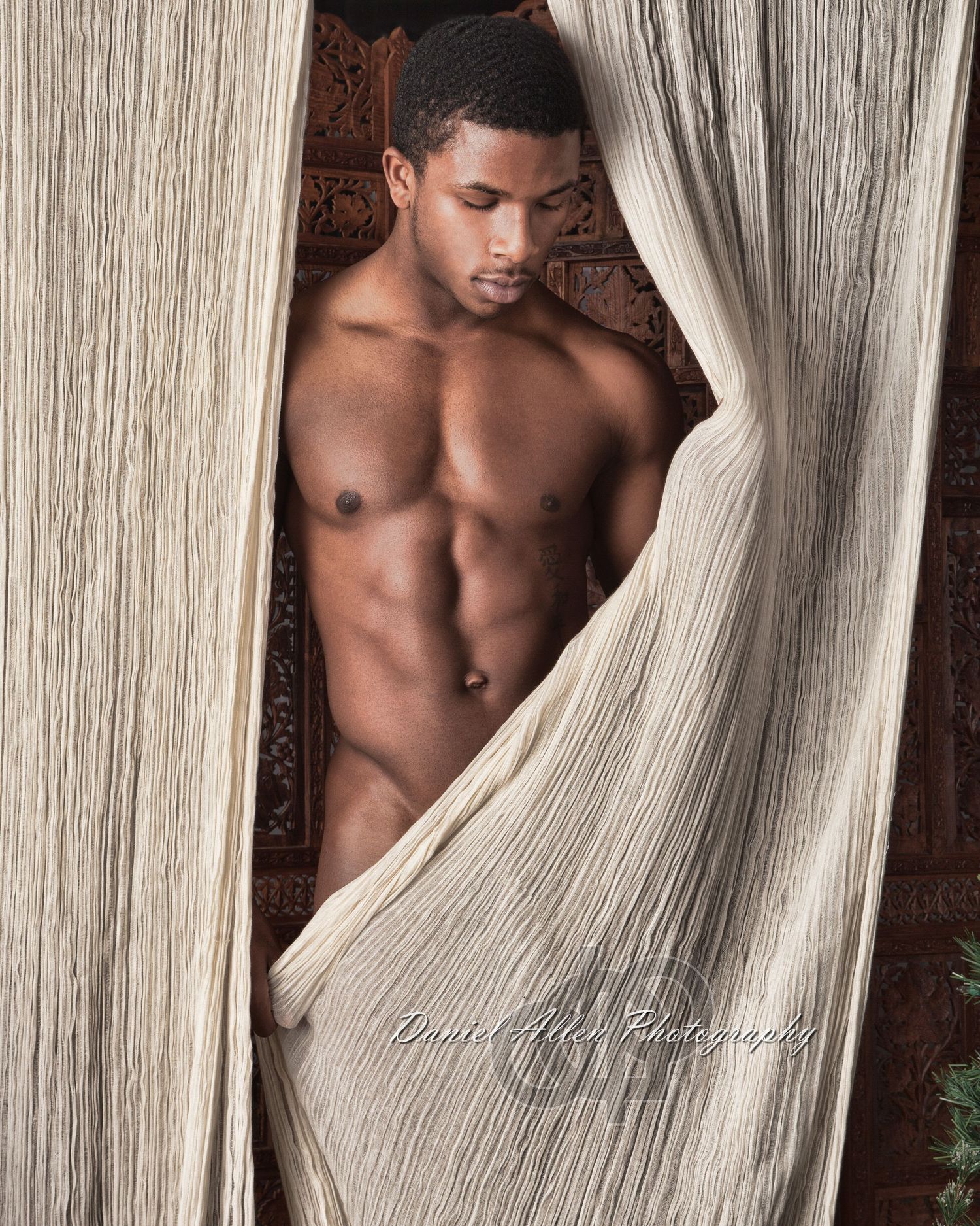 Figure poses artistically behind flowing white fabric in studio setting.