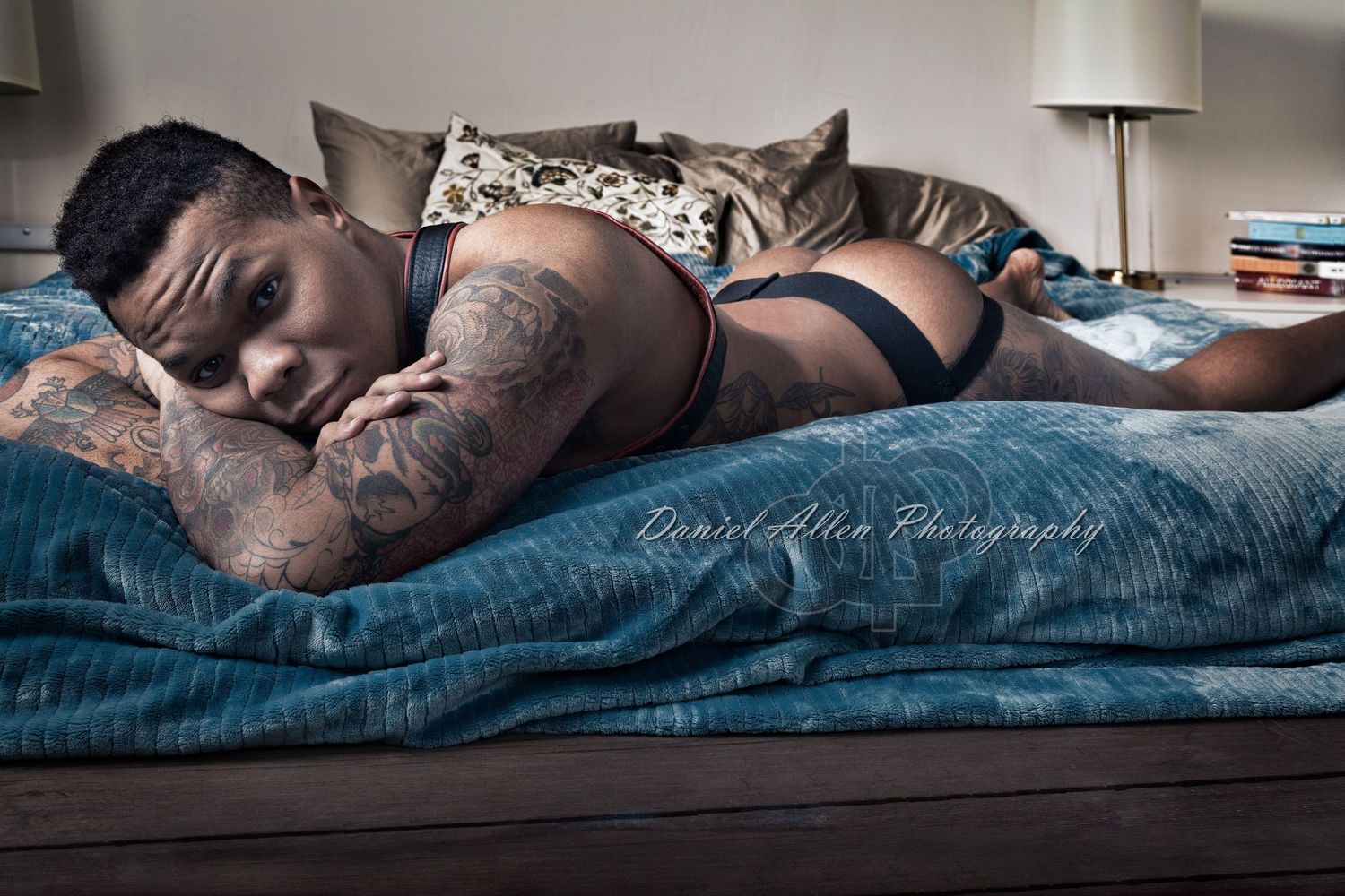 Artistic boudoir photo with soft lighting and blue tones showing a figure reclining on dark bedding.