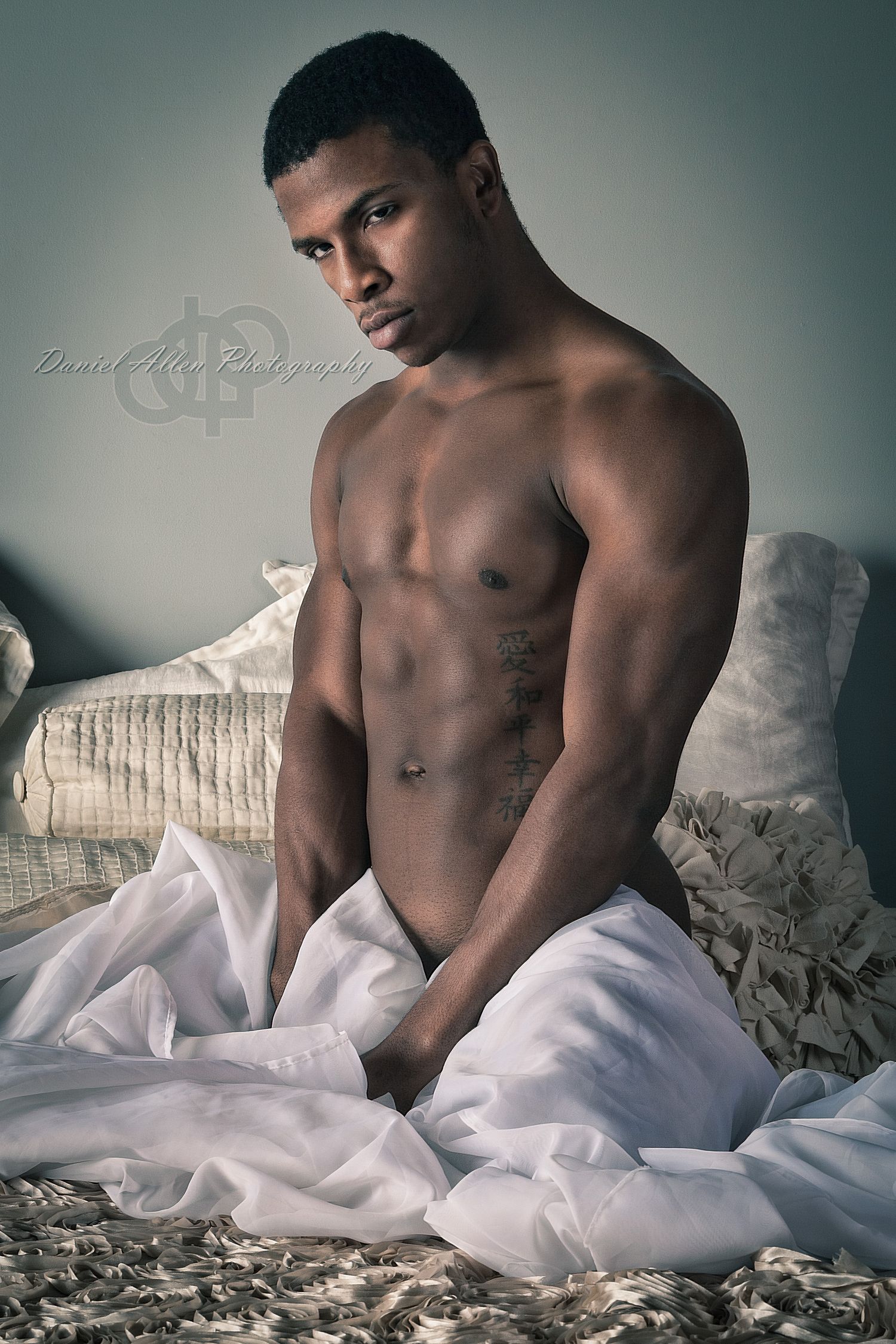 Artistic boudoir photo featuring model draped in white sheets against textured pillows.