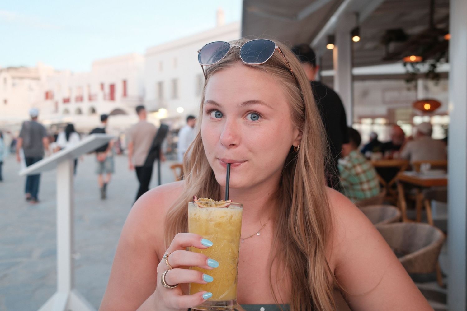 Young woman sipping an orange frozen drink through a straw at an outdoor cafe in Mykonos, Greece.