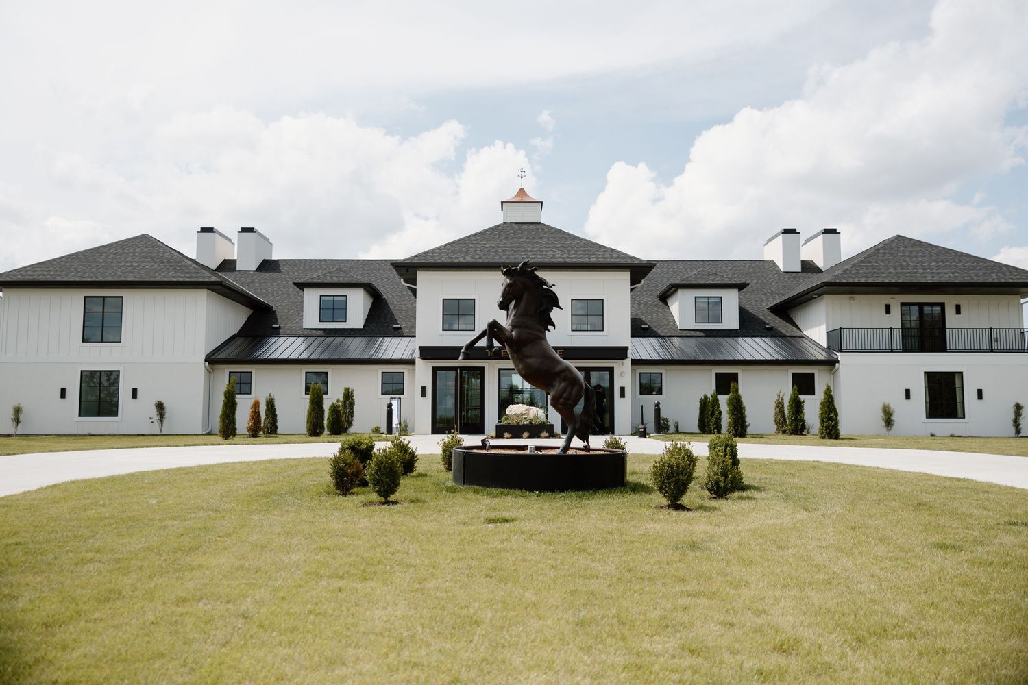 A panoramic view of a modern white ranch-style house with dark roof and multiple chimneys on a green lawn.