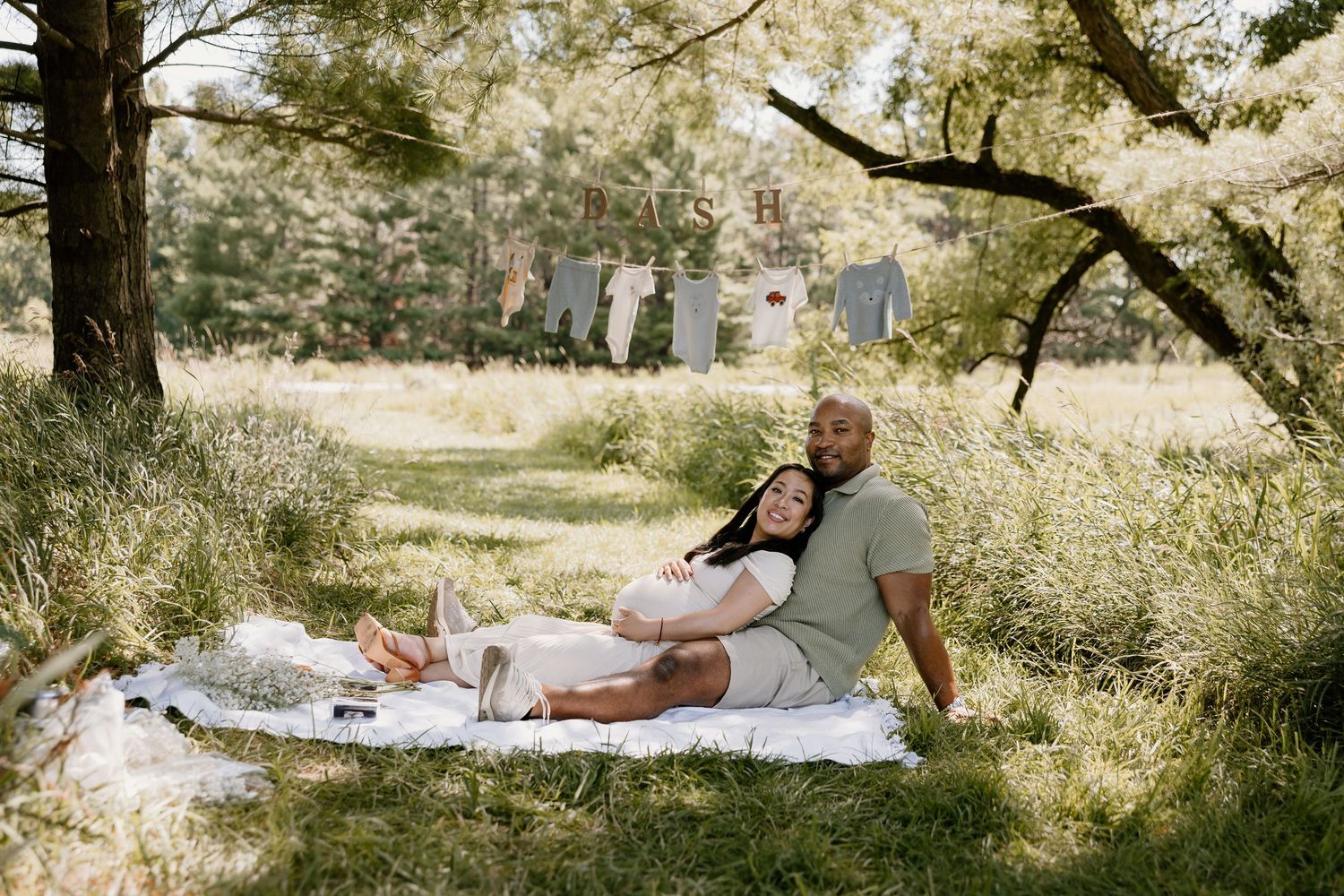 Couple relaxing on blanket during outdoor photoshoot with trees in background.