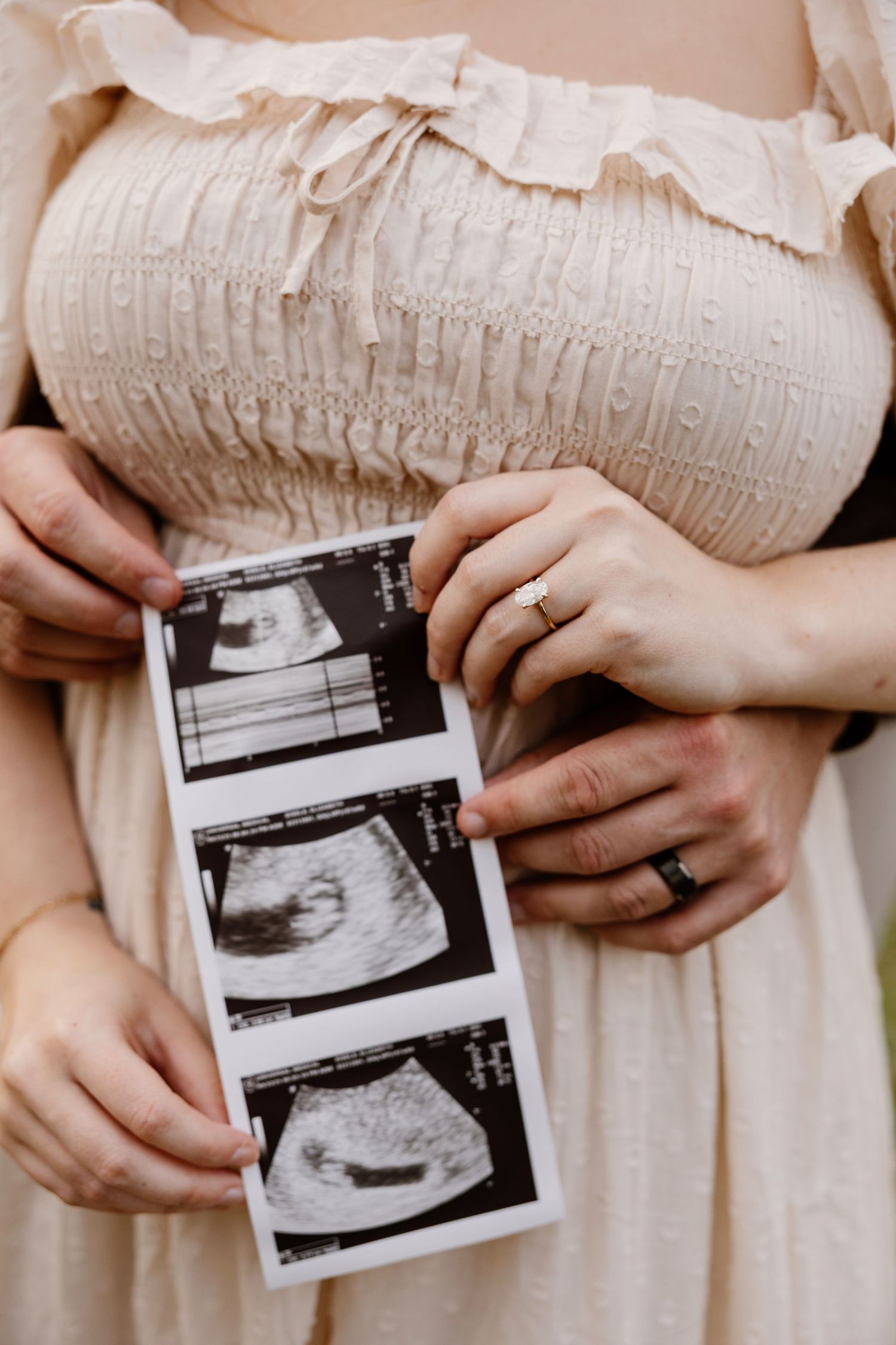 Hands holding black and white ultrasound photos against cream-colored dress.