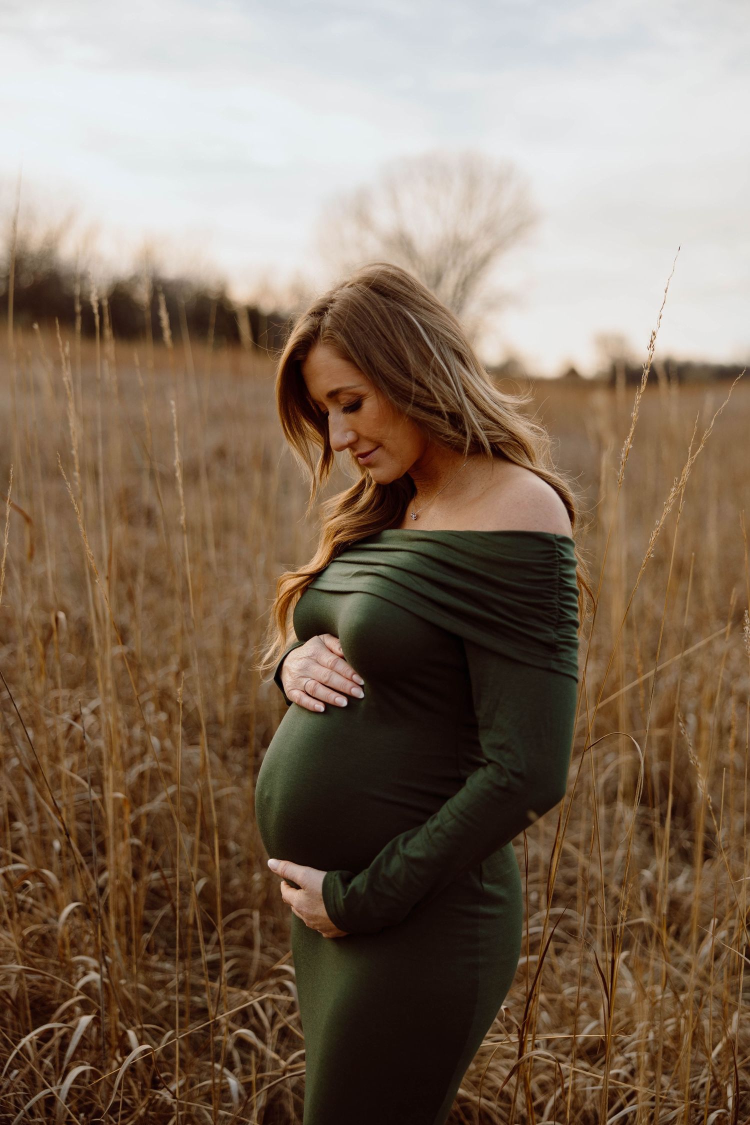 Maternity portrait in tall grass field during golden hour.
