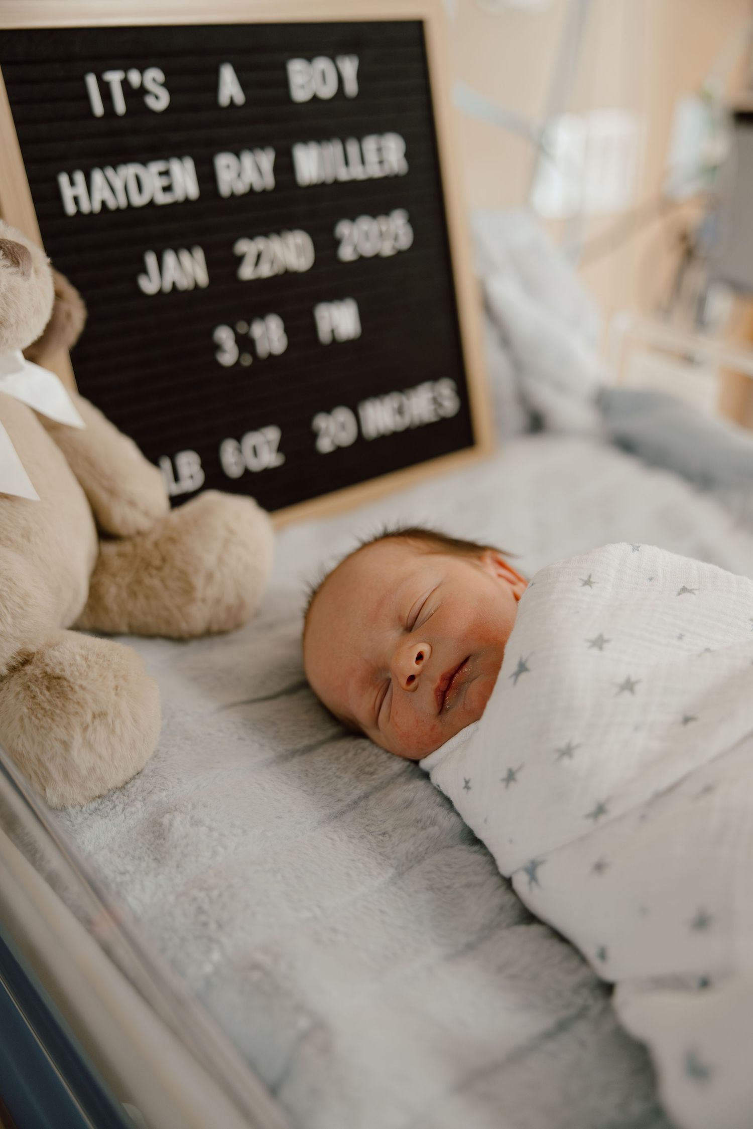 Newborn resting in hospital bassinet with birth announcement letterboard.