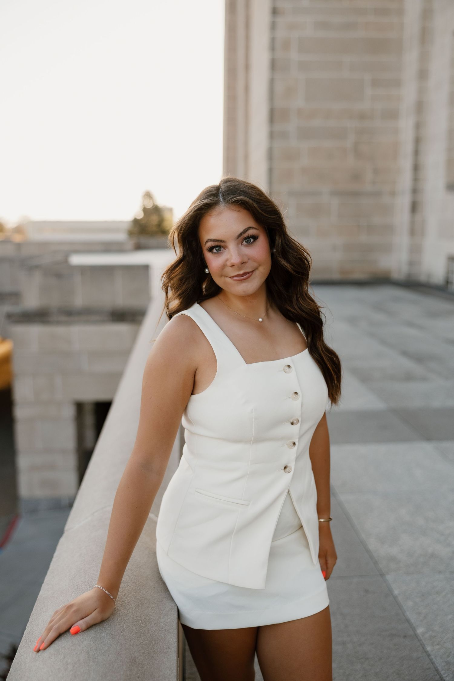 A person wearing a stylish white button-front sleeveless dress poses outdoors during golden hour.