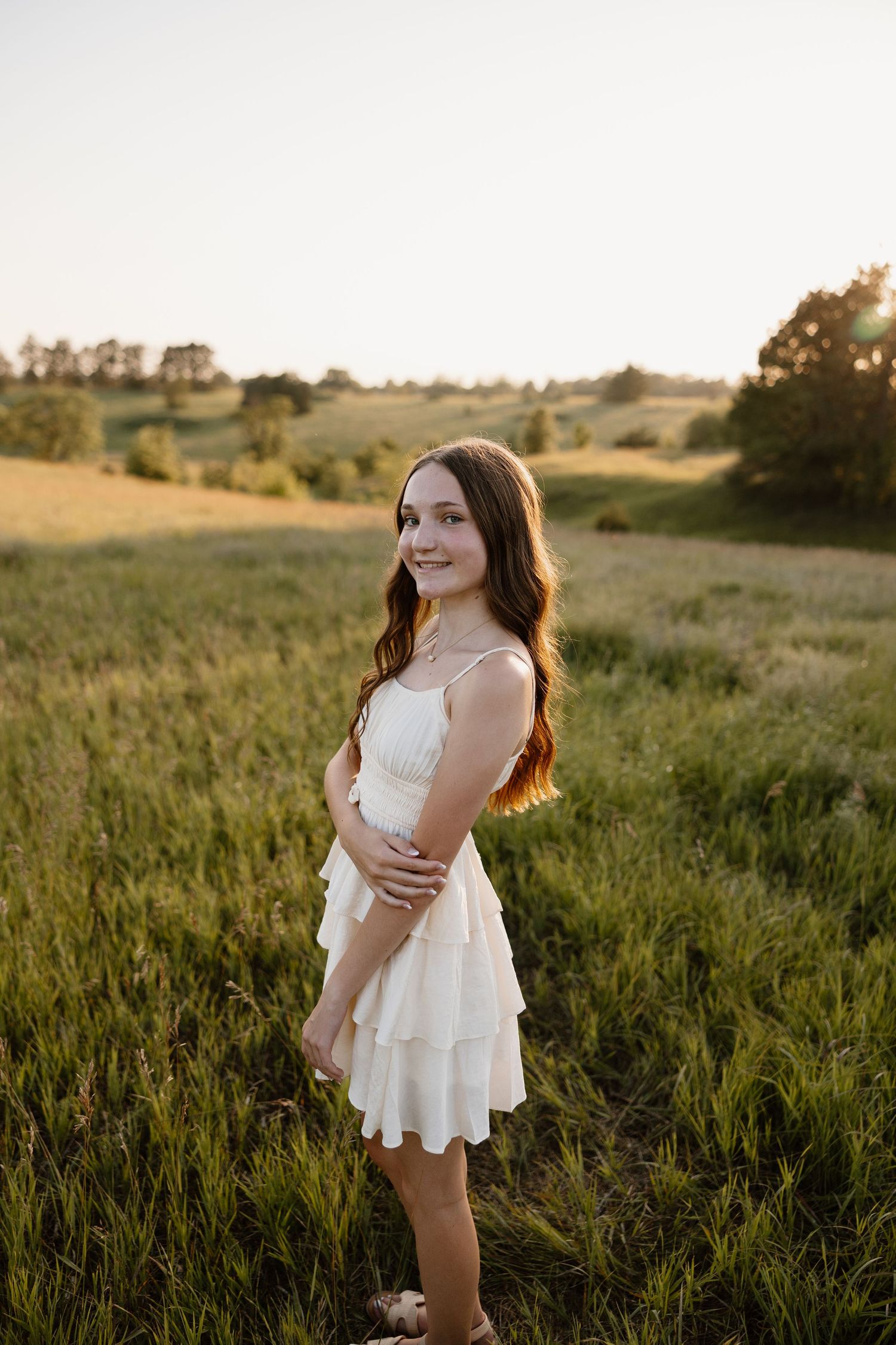 Young woman in white dress twirling in a sunlit meadow at sunset.