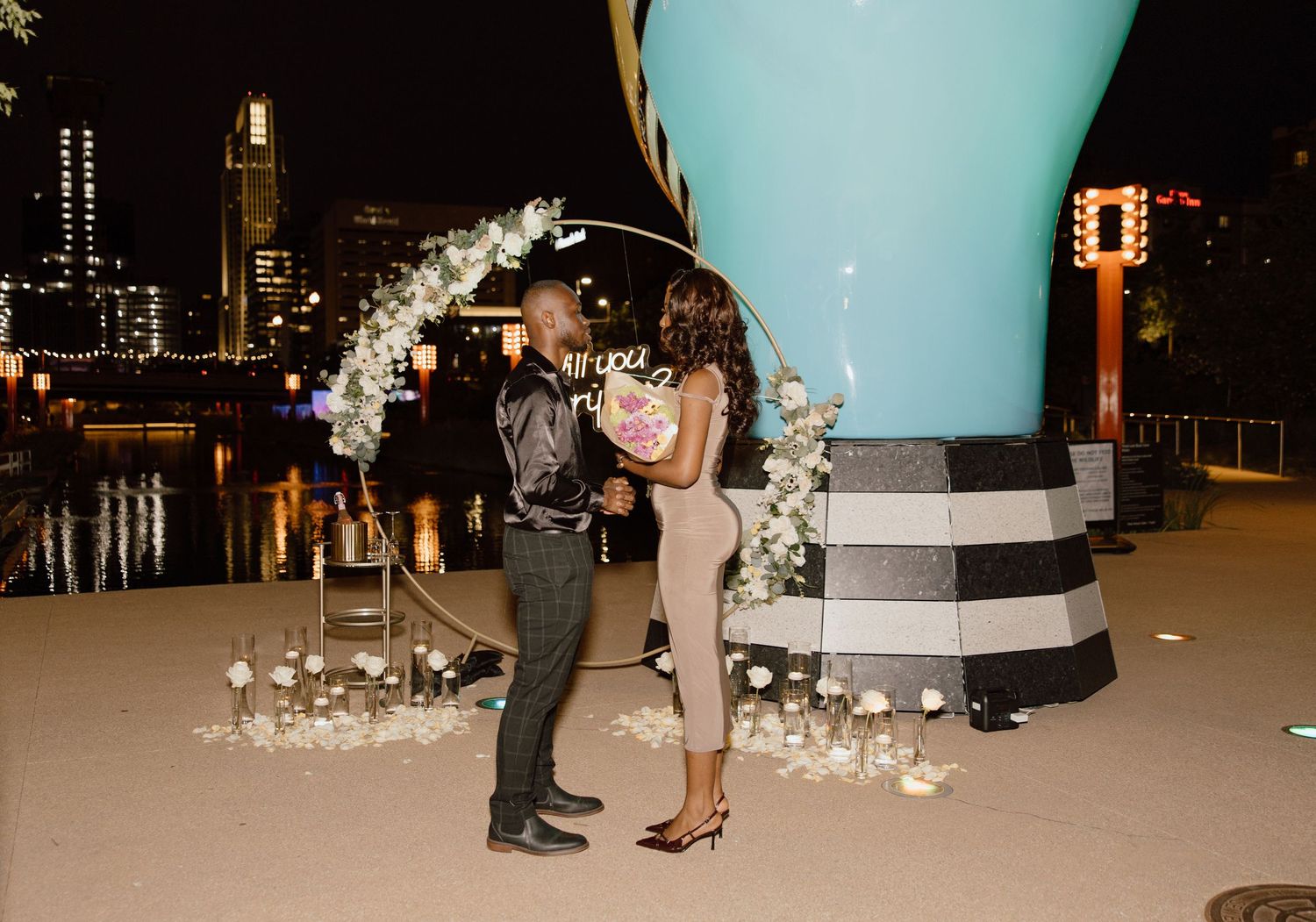 A romantic rooftop proposal setup with city lights and floral arrangements.