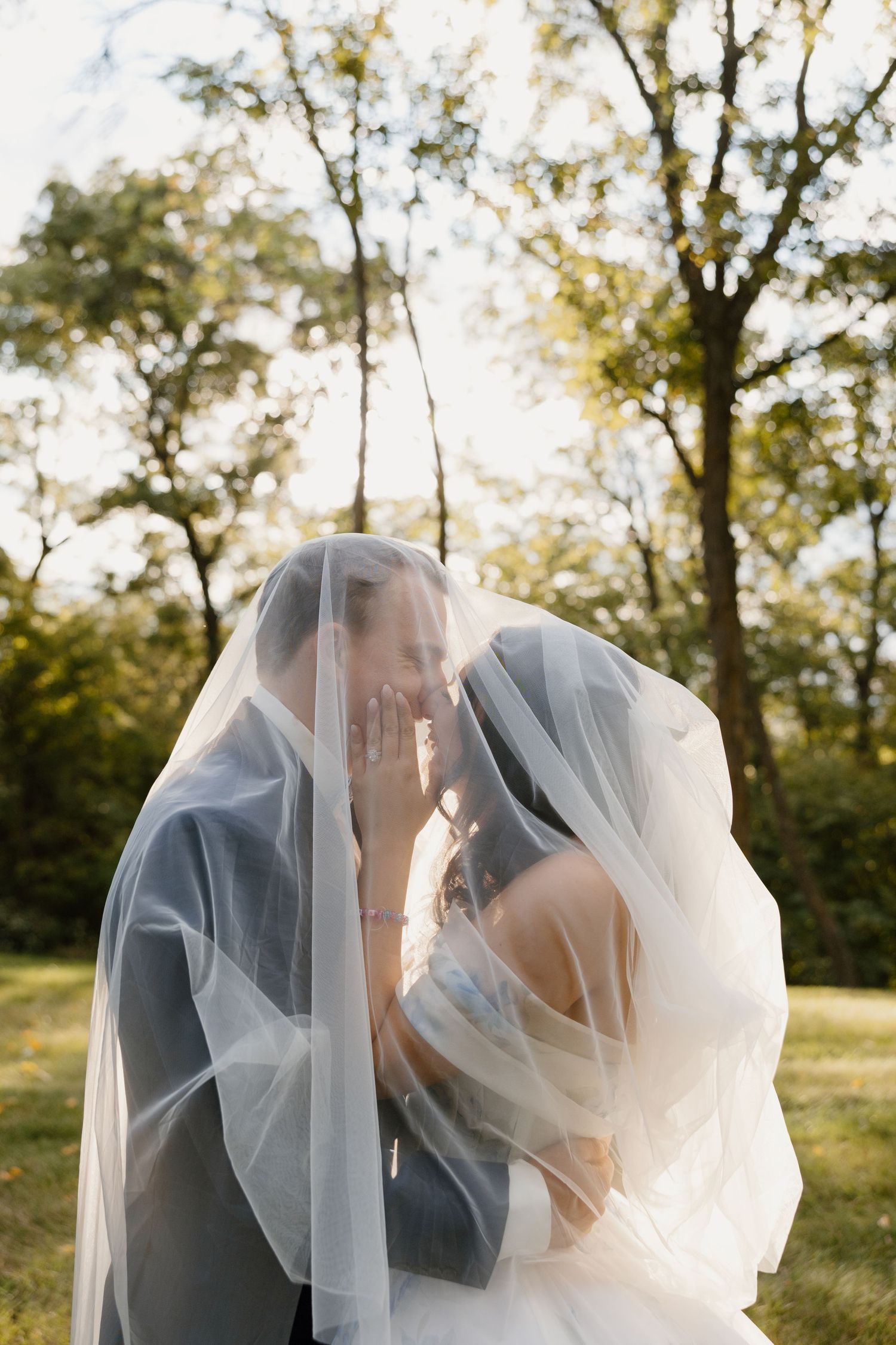 Romantic veil shot of couple under trees during outdoor wedding.