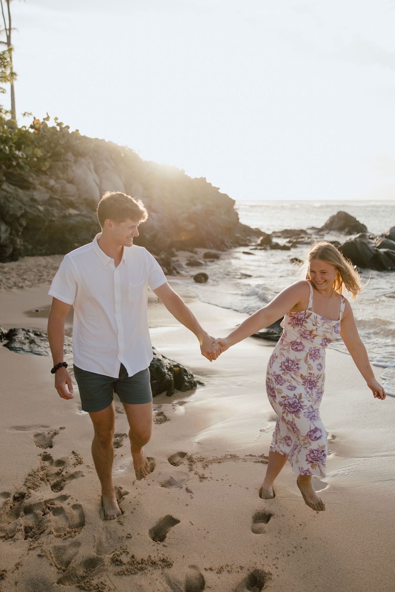 A romantic beach scene at sunset with rocky coastline and waves in the background.