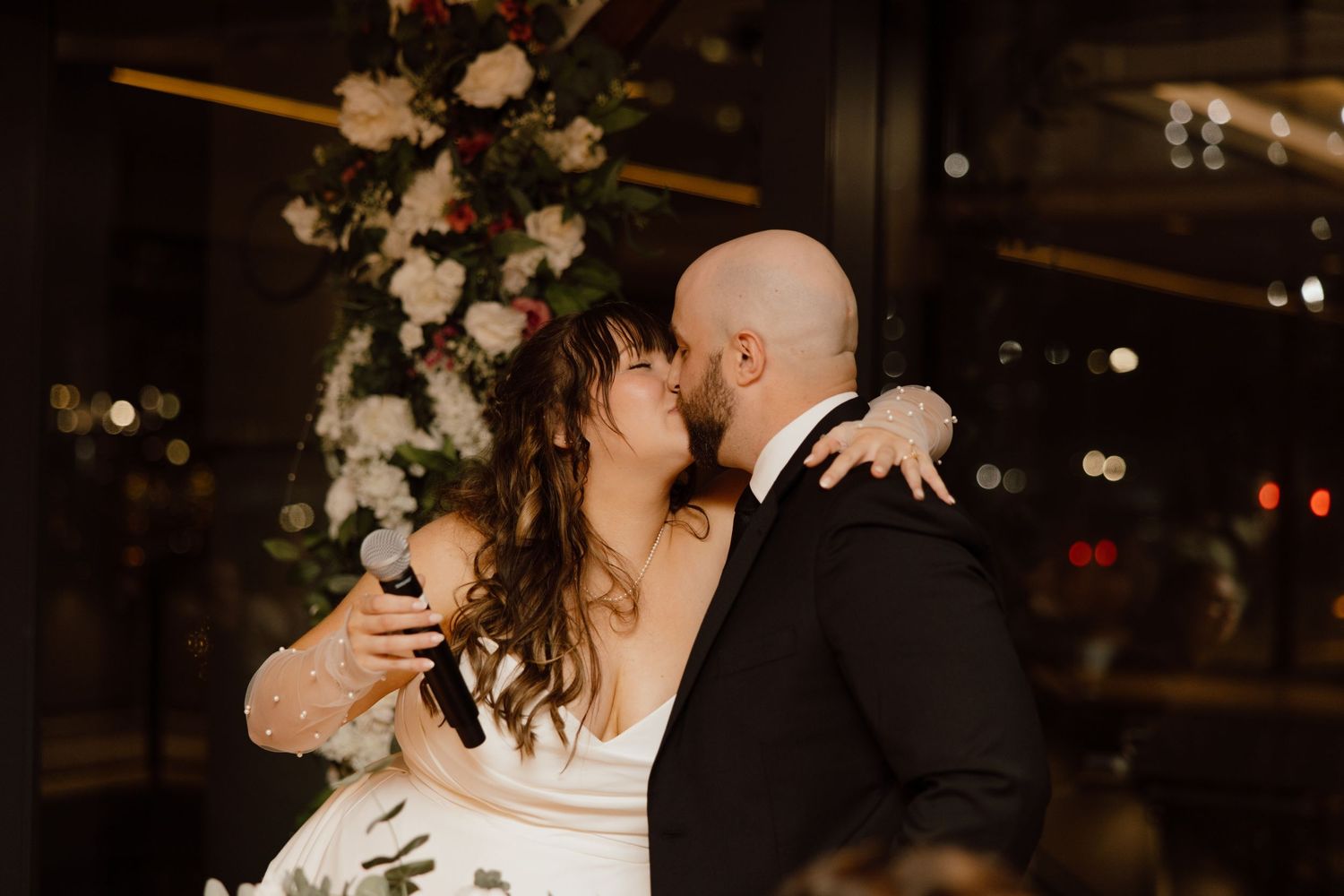A couple shares an intimate moment during their wedding celebration with wine glasses in hand.
