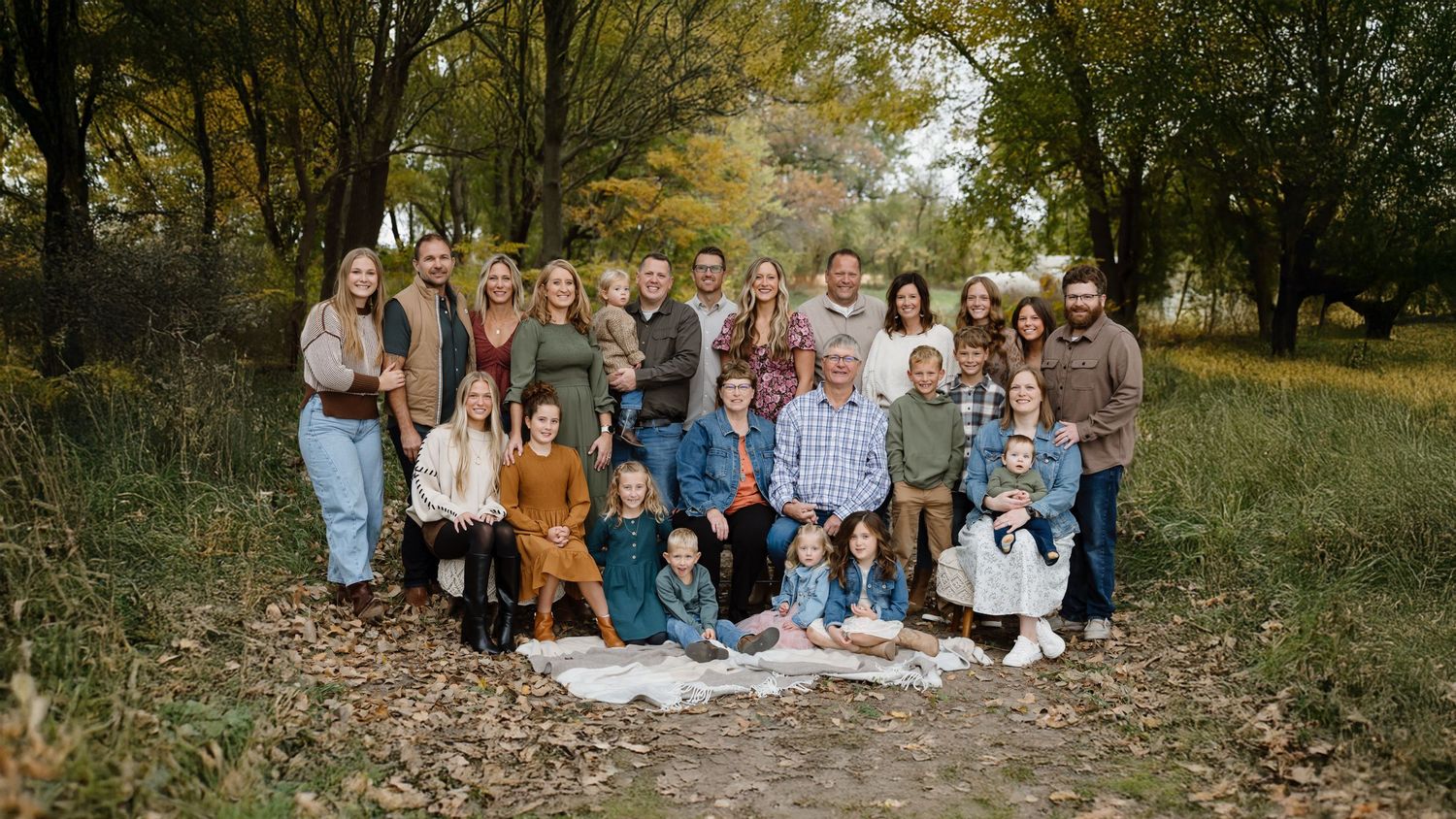 Large group portrait taken outdoors in autumn with fall foliage and trees in the background.