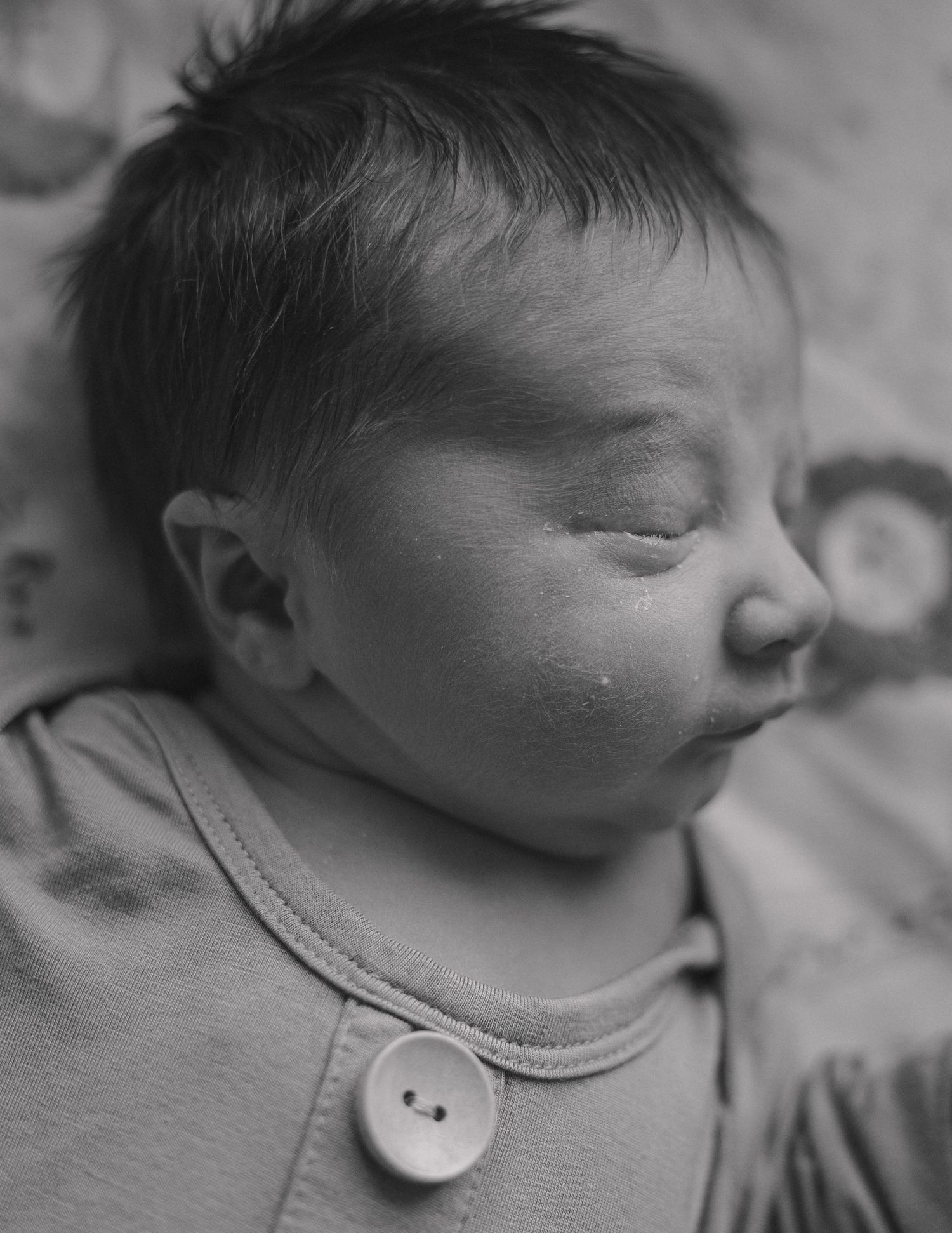 A peaceful sleeping newborn wearing a light colored onesie with a large button detail in black and white photography.