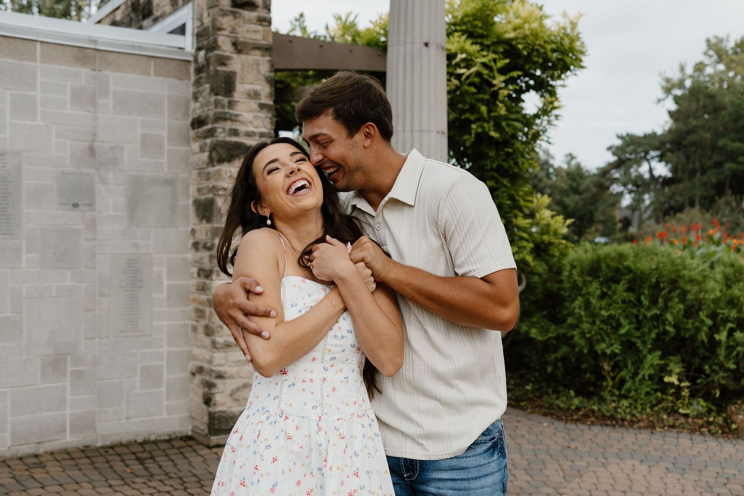 A couple shares joyful moments together against stone pillars and greenery.