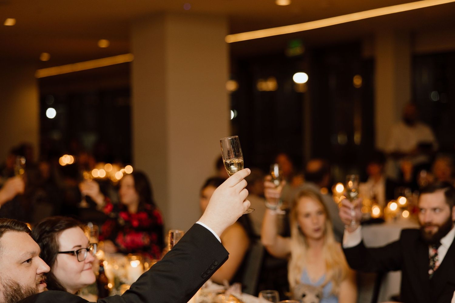 Wedding guests raise their glasses in a celebratory toast during an evening reception.