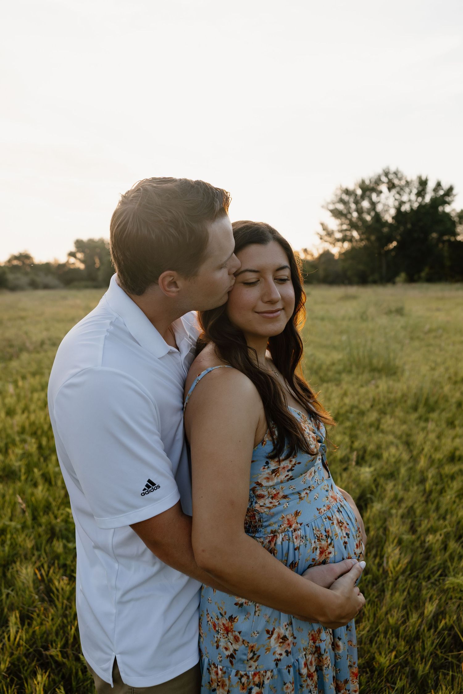 Couple embracing in a sunny field during sunset pregnancy announcement photoshoot.