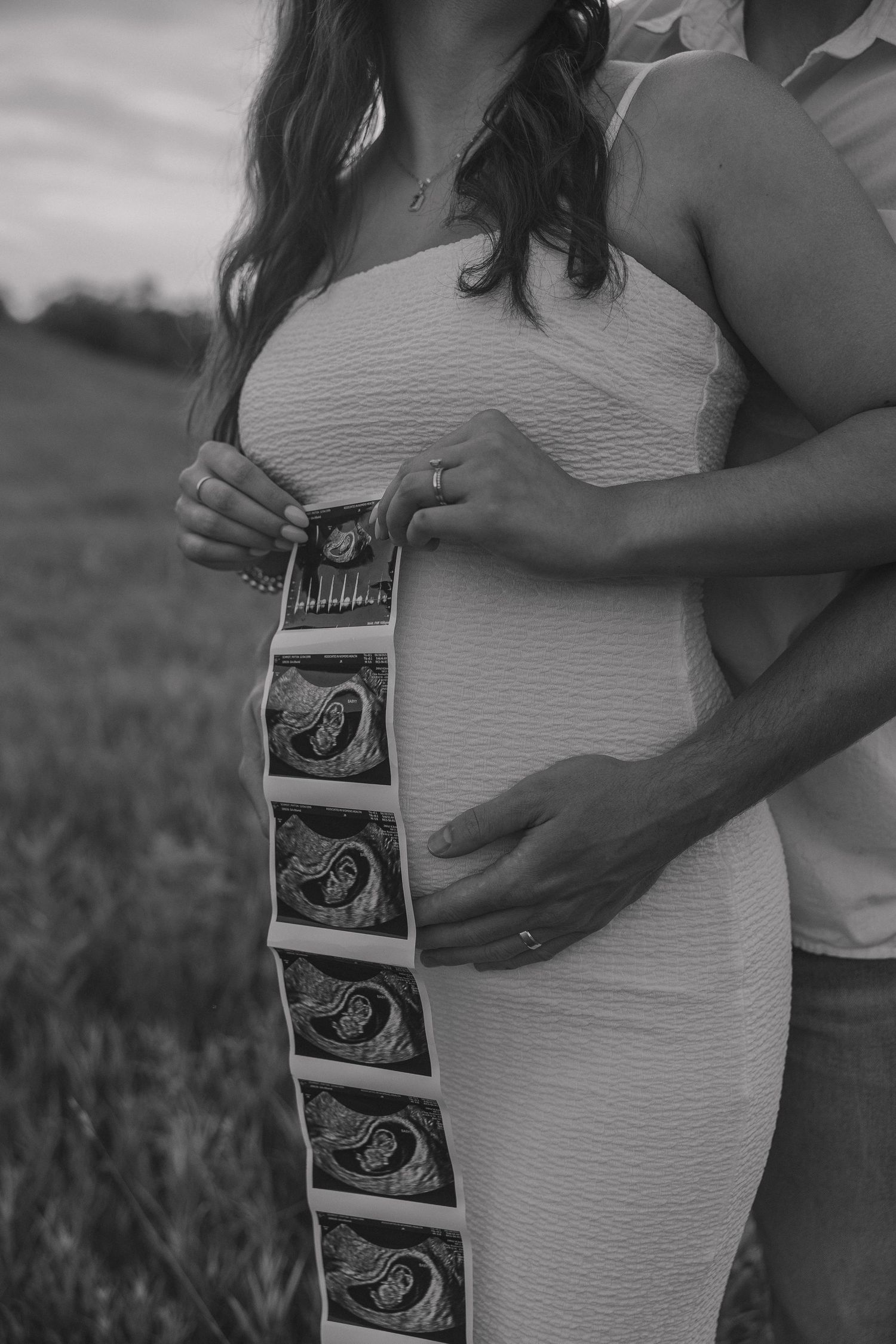 Black and white photo of couple holding ultrasound images in field.