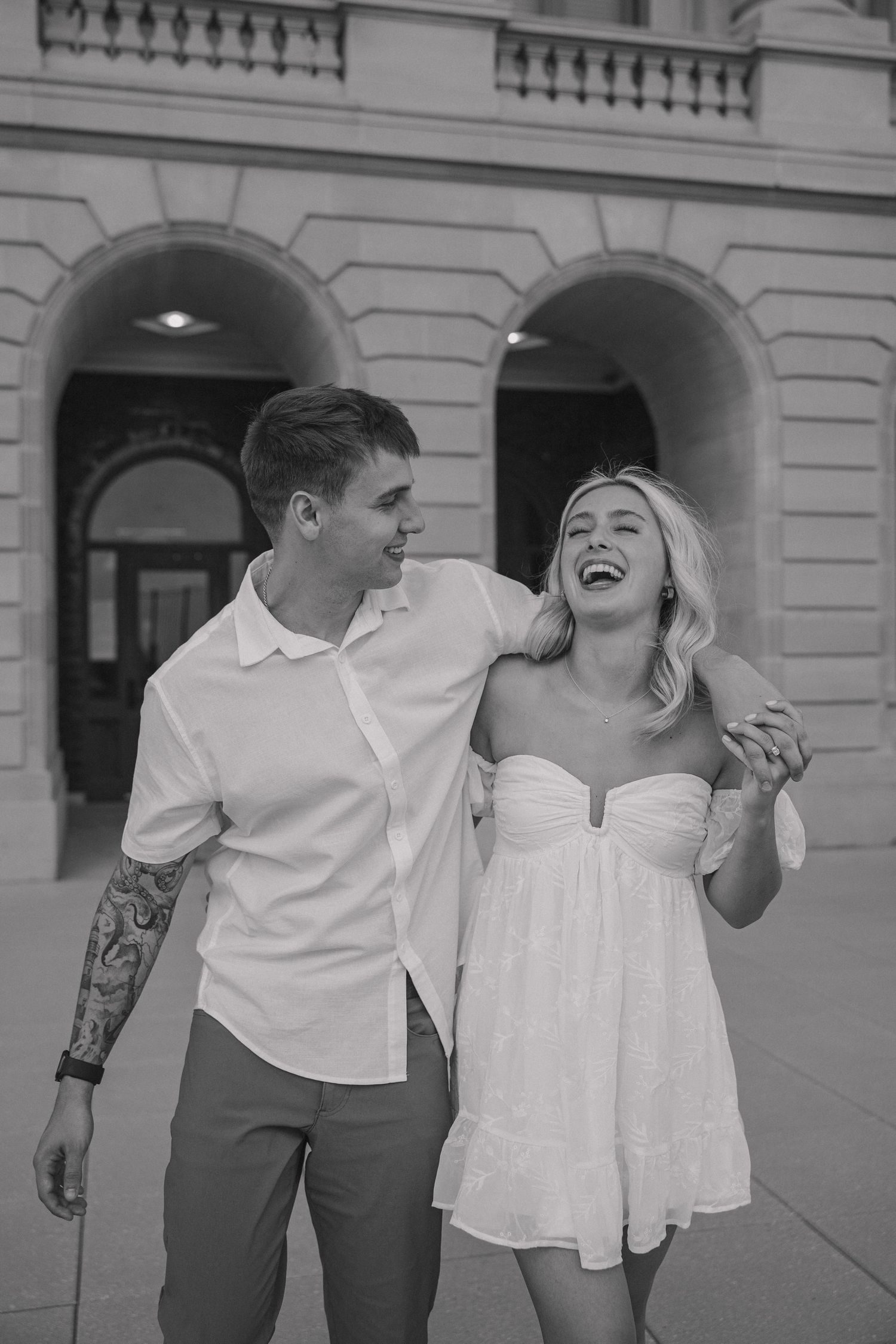 A candid black and white photo of a couple laughing together outside a classic building.
