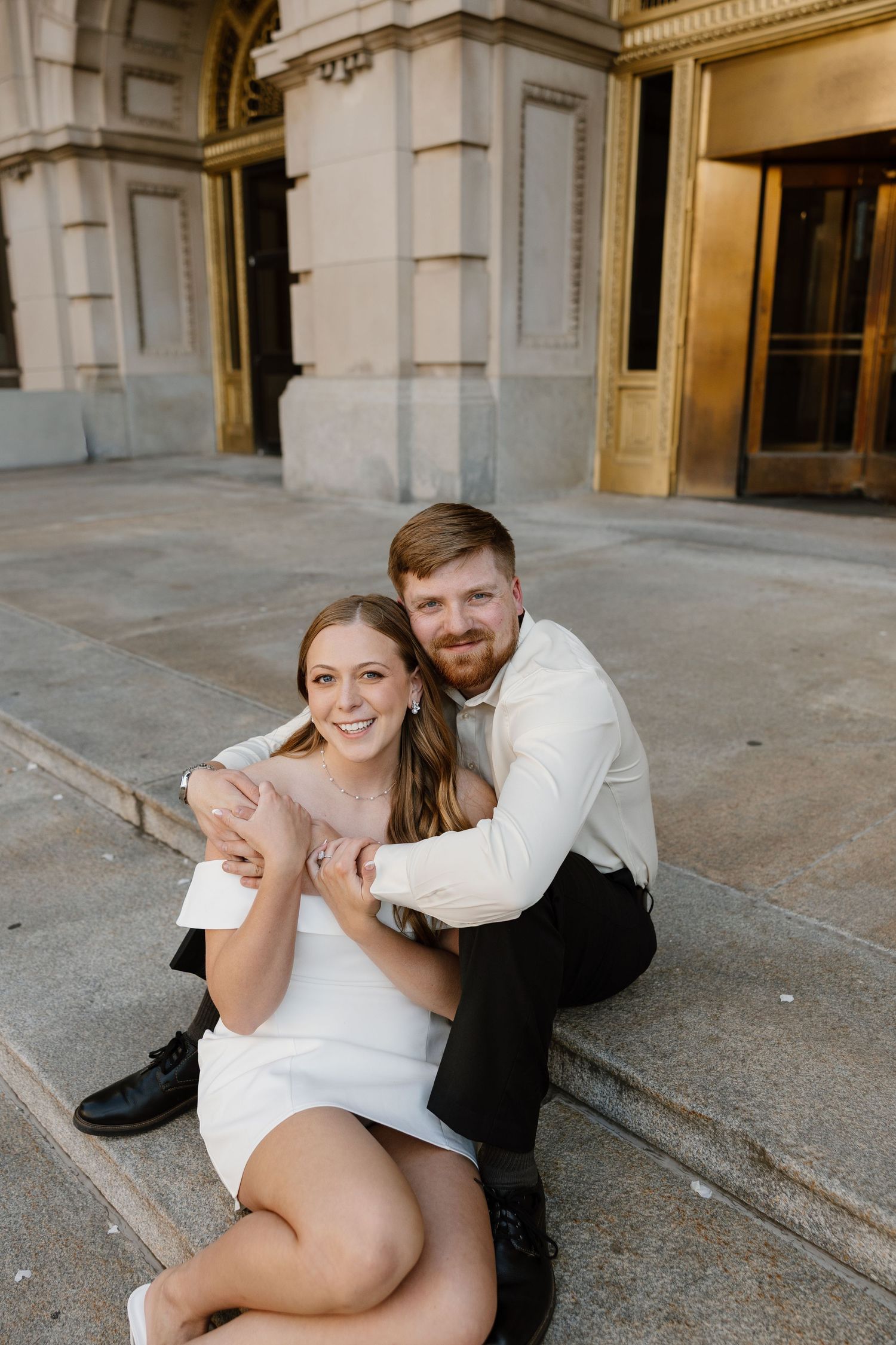 Couple shares playful moments on grand stone steps of historic building during photo session.