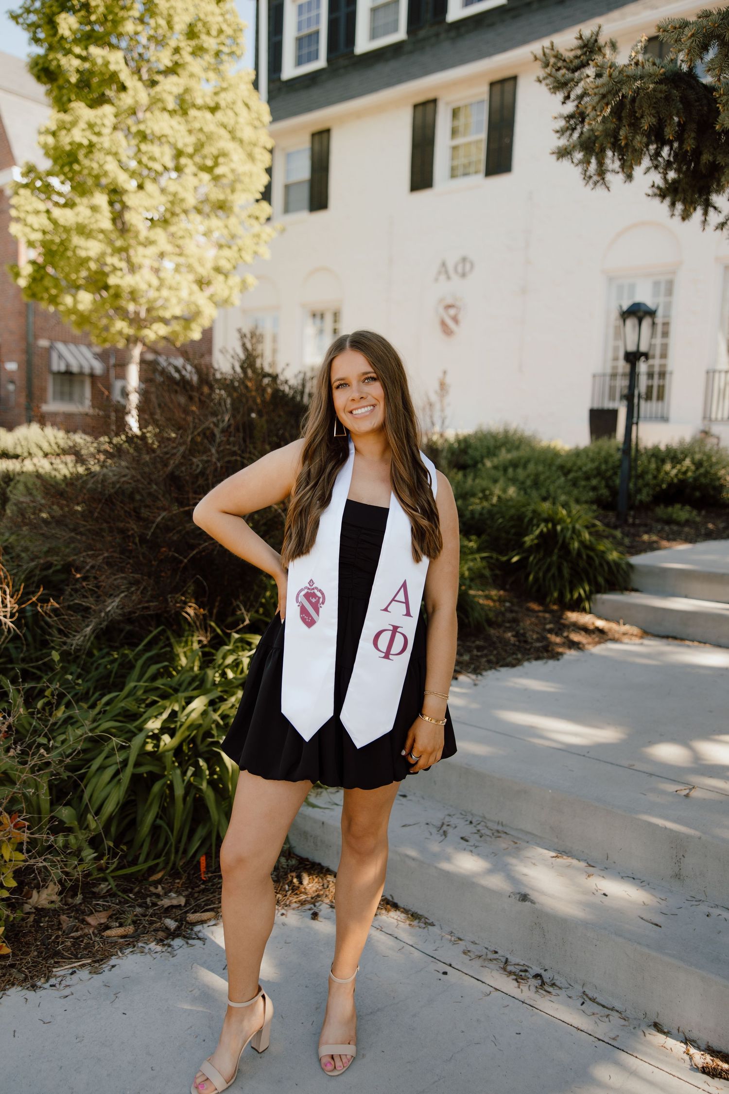 Graduate wearing stole and black dress poses near campus buildings.